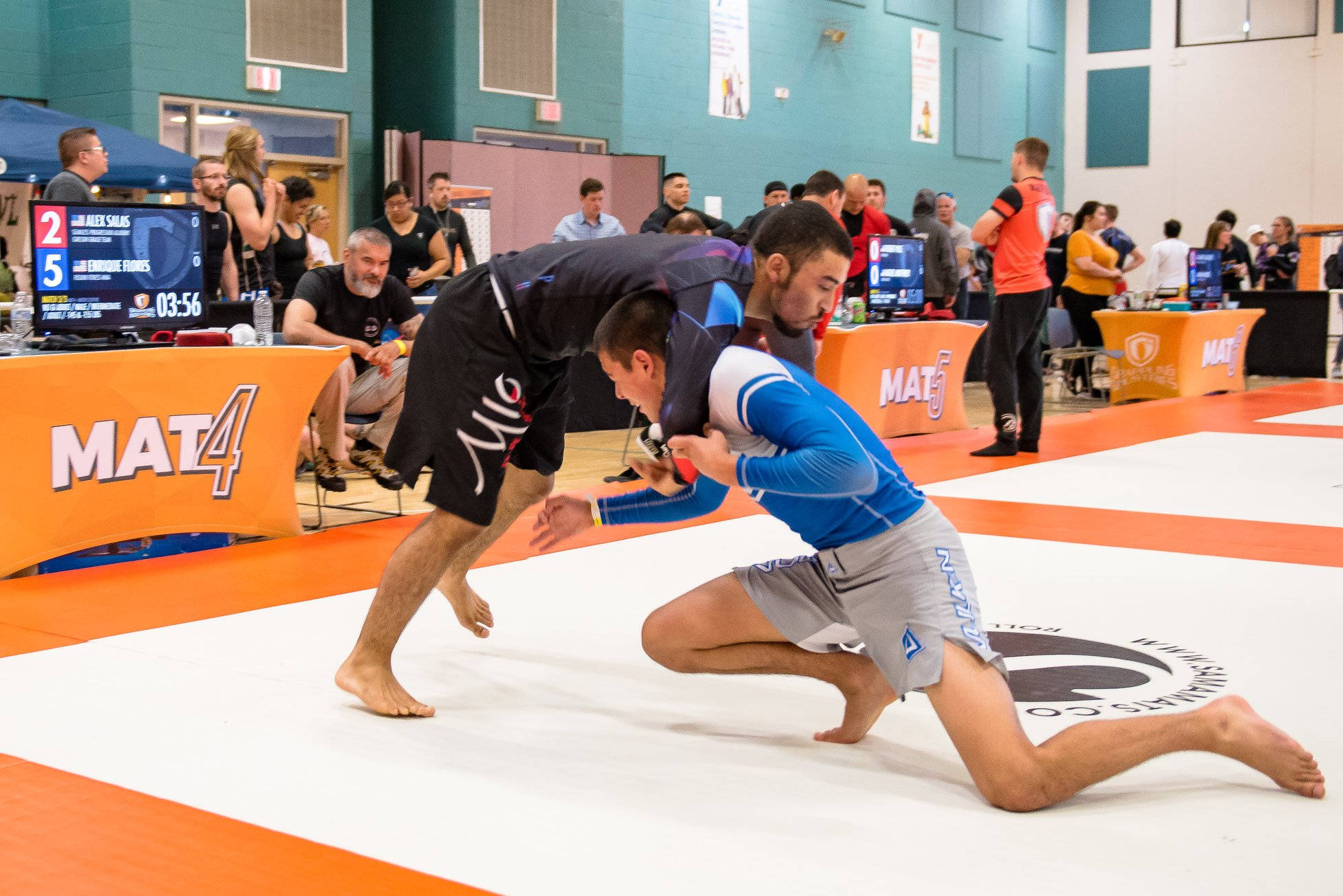 martial arts 桌布 壁紙 — 兩名男性運動員在體育館的白色和橙色摔角墊上激烈纏鬥，進行一場競技比賽。