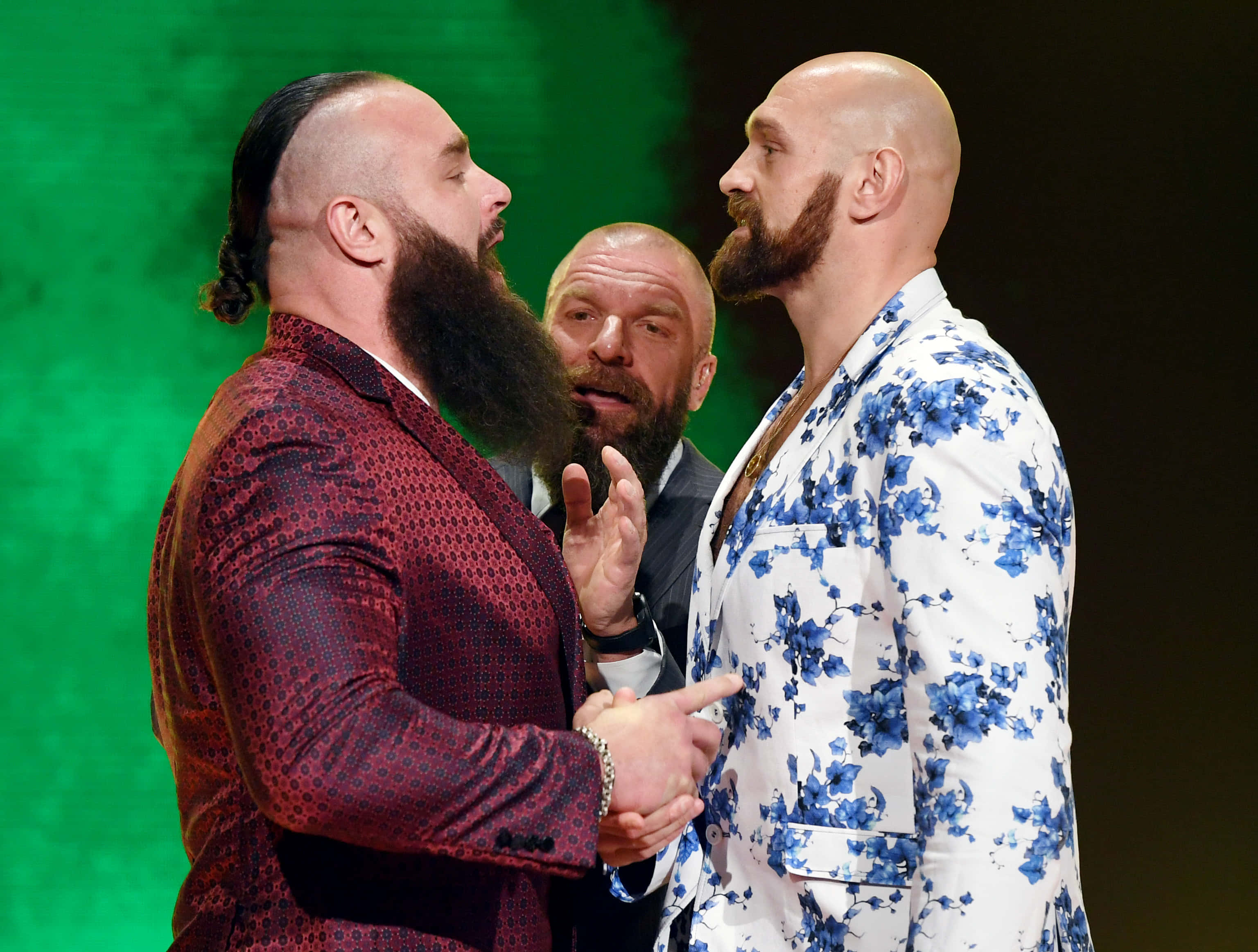 WWE 桌布 壁紙 — 兩名留鬍子的摔角手穿著大膽圖案西裝，在綠色舞台燈光下對峙，中間有一名裁判。