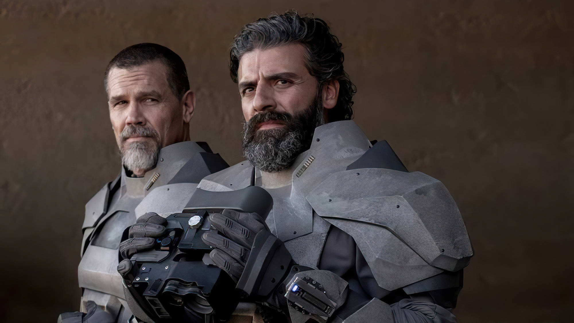 Dune 2021 桌布 壁紙 — 兩名留鬍鬚的男子身穿未來風格的灰色盔甲，在帶有紋理的棕色背景前神情嚴肅地站立。
