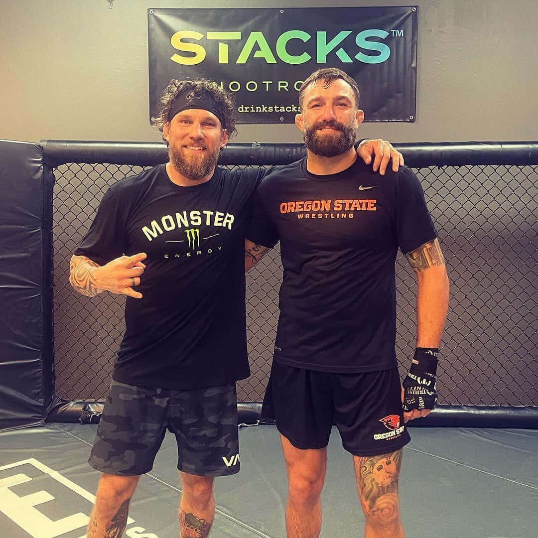 UFC 桌布 壁紙 — 兩名留鬚男子身穿摔角裝備，在MMA籠內自信擺姿勢，身後有「STACKS」橫幅。