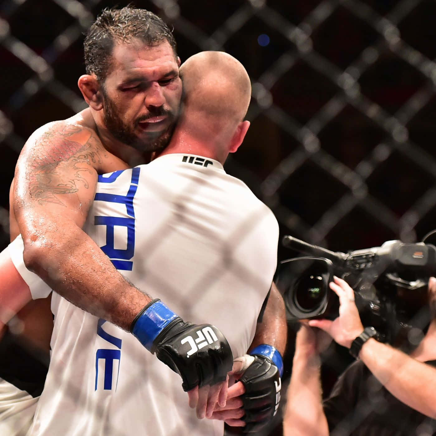 MMA 桌布 壁紙 — 兩名疲憊的UFC拳手在明亮的場館燈光下，於八角籠內真誠地擁抱。