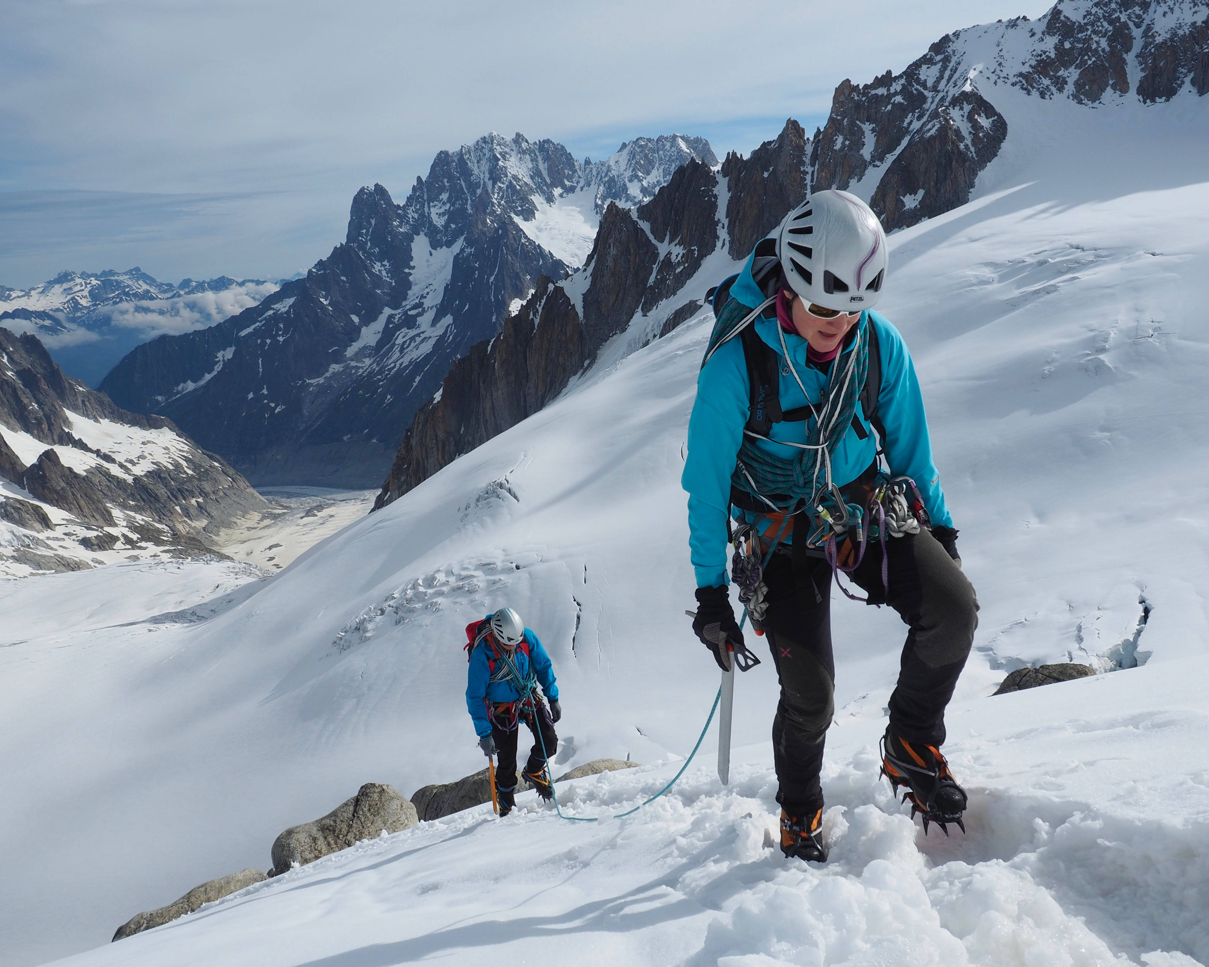 Climbing 桌布 壁紙 — 兩名登山者在晴朗的天空下，以冰斧和冰爪攀登積雪的山坡，背景是鋸齒狀的山峰。