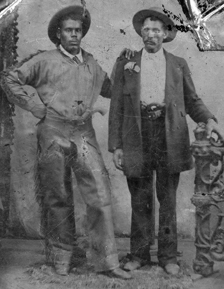 Old Western 桌布 壁紙 — 兩名穿著復古服裝的男子在一個風化的工作室肖像中正式擺姿勢，配有華麗的道具和可見的膠片損壞。