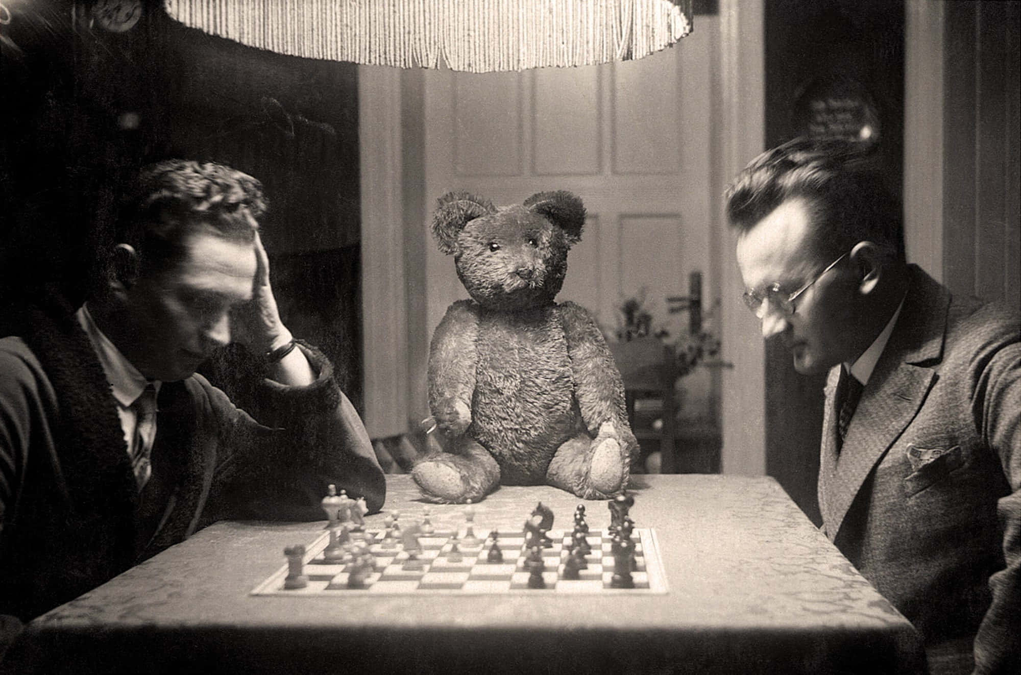Teddy Bear 桌布 壁紙 — 兩名穿著復古西裝的男子在流蘇燈下激烈下棋，中間坐著一隻破舊的泰迪熊。