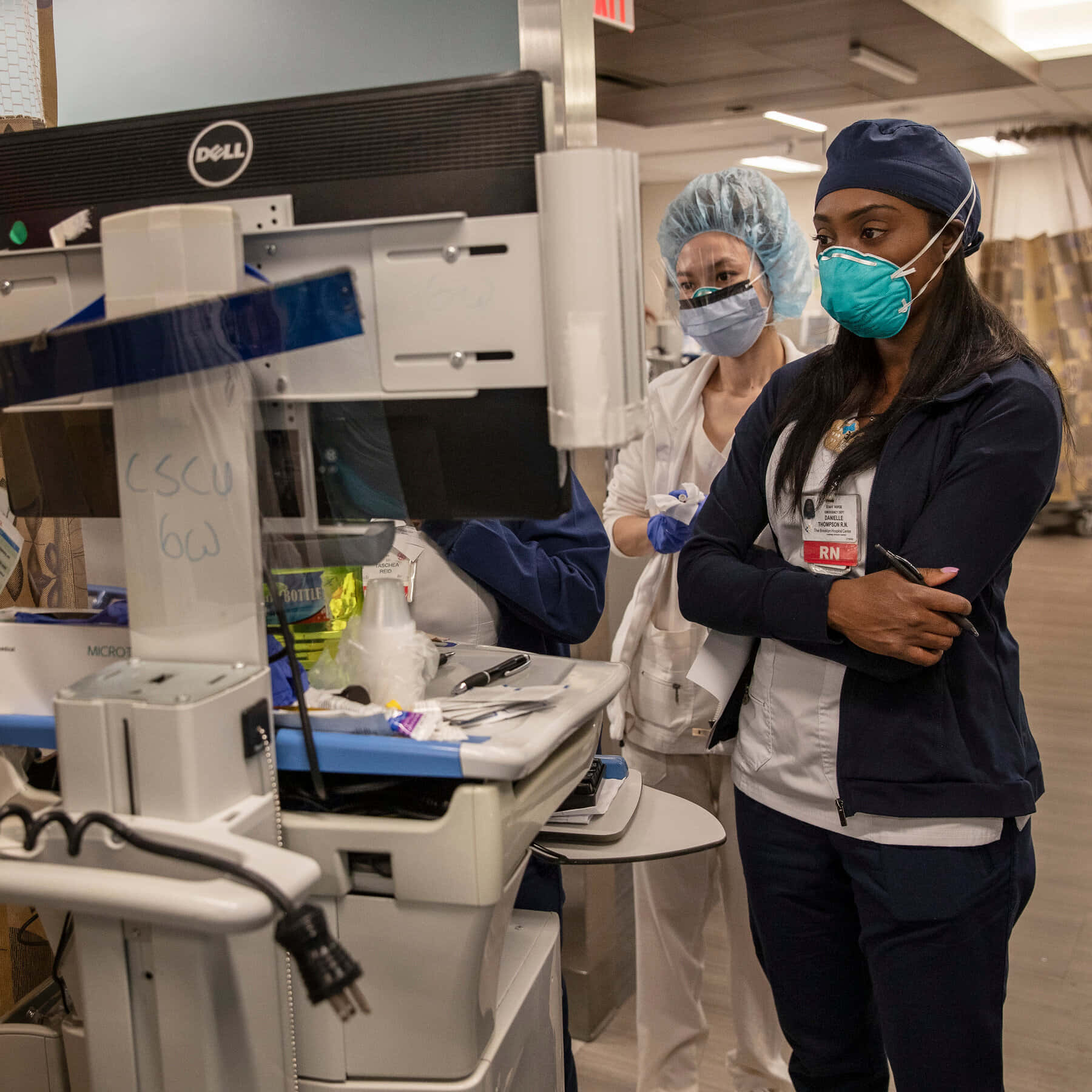 Nursing 桌布 壁紙 — 兩名穿著手術衣、口罩和帽子的醫護人員在醫院環境中專注地站在醫療設備附近。