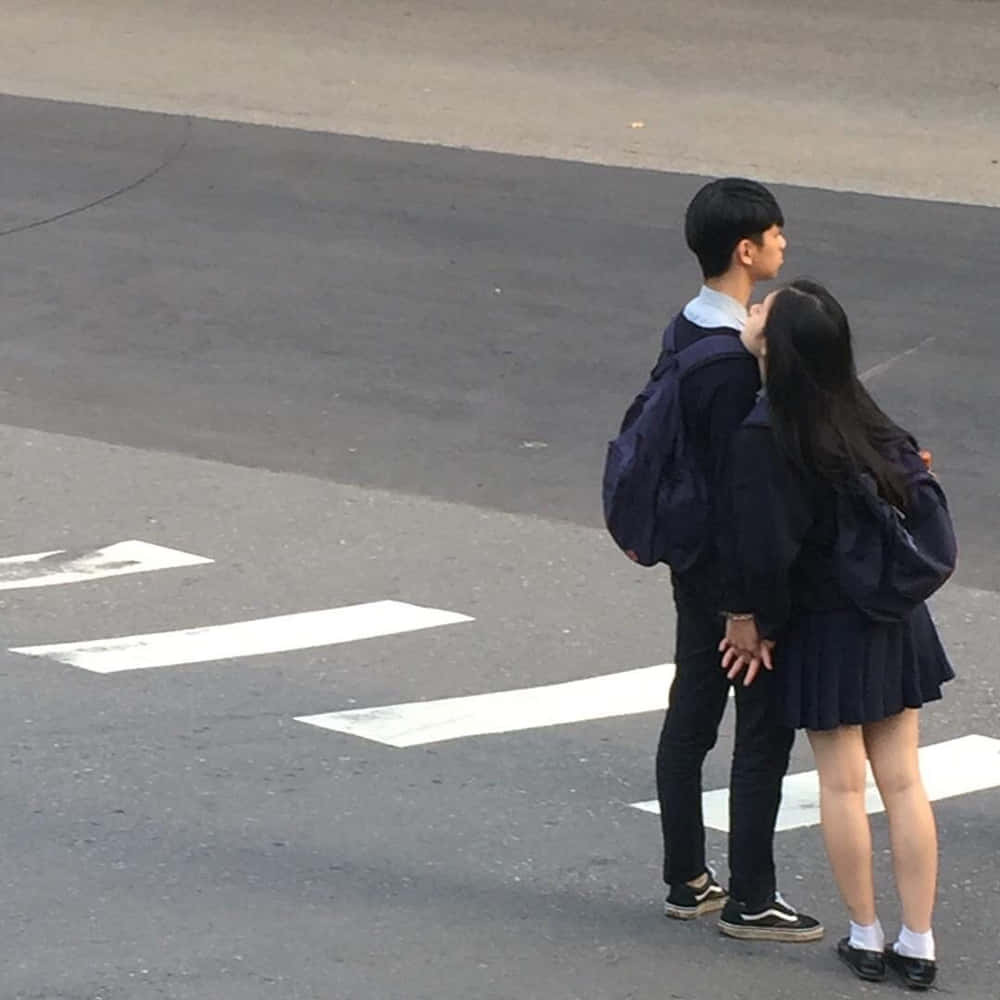 情侶 桌布 壁紙 — 兩名穿著校服的學生在行人穿越道上緊密地站著，手牽手一起向前凝視。