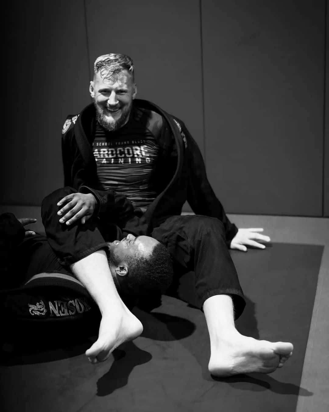 Athletic 桌布 壁紙 — 兩名穿著格鬥裝備的男子在訓練墊上分享歡樂時刻，照片為清晰的黑白風格。
