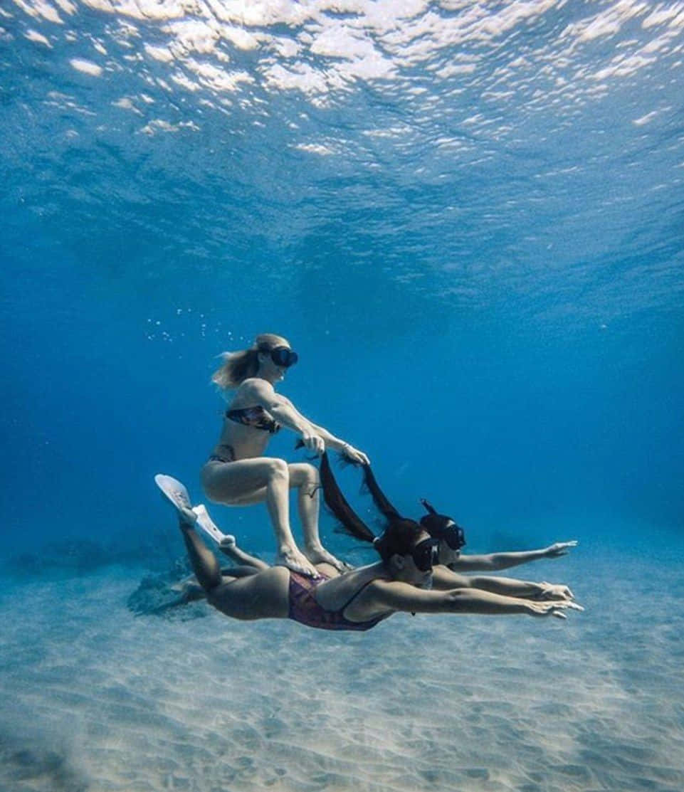 海洋 桌布 壁紙 — 兩名穿著浮潛裝備的女性在沙質海床上優雅地滑行，其中一人騎在另一人身上。