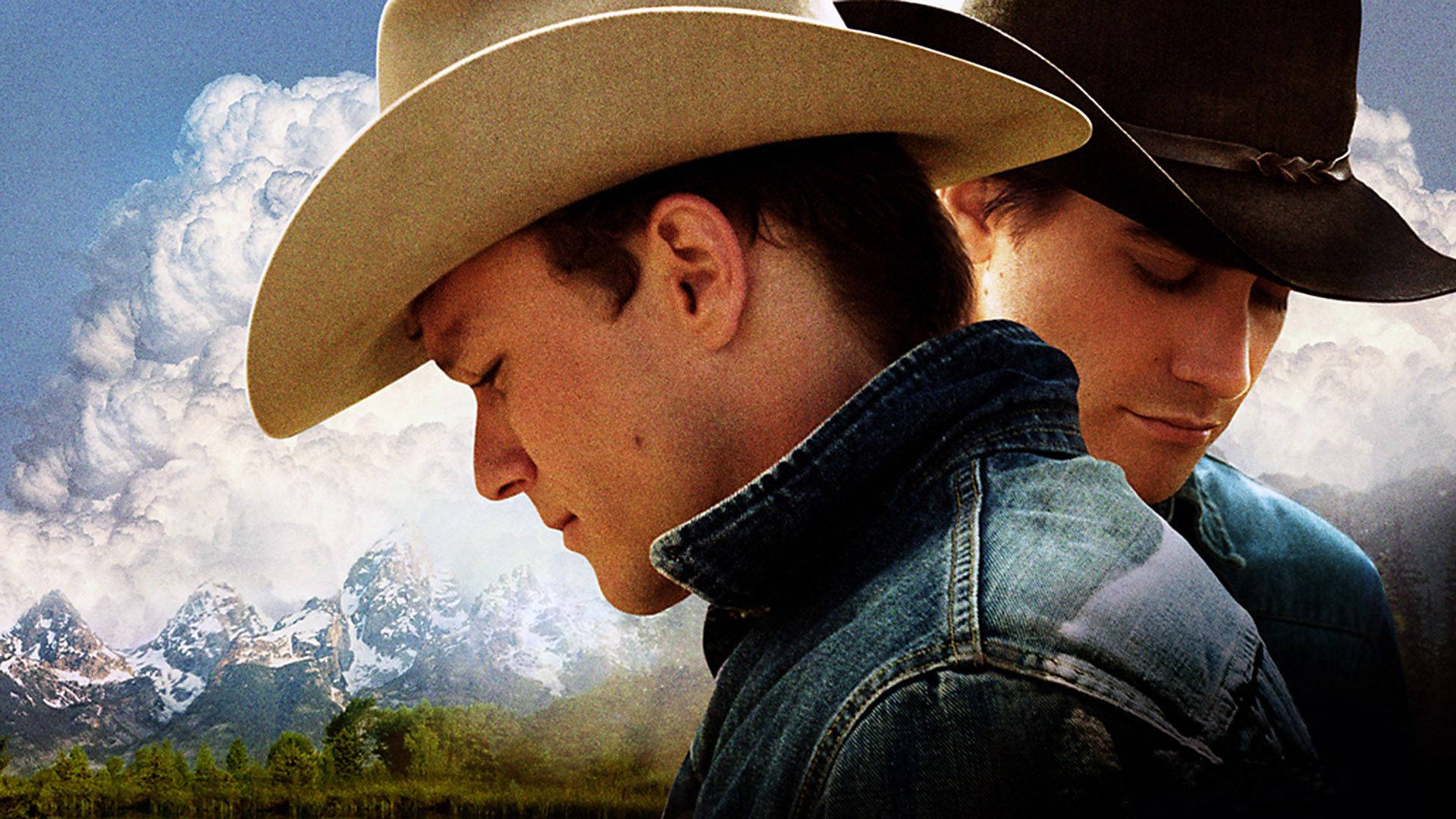 brokeback mountain 桌布 壁紙 — 兩名穿著牛仔外套和帽子的牛仔，在白雪覆蓋的山脈和戲劇性的雲層背景下向下凝視。