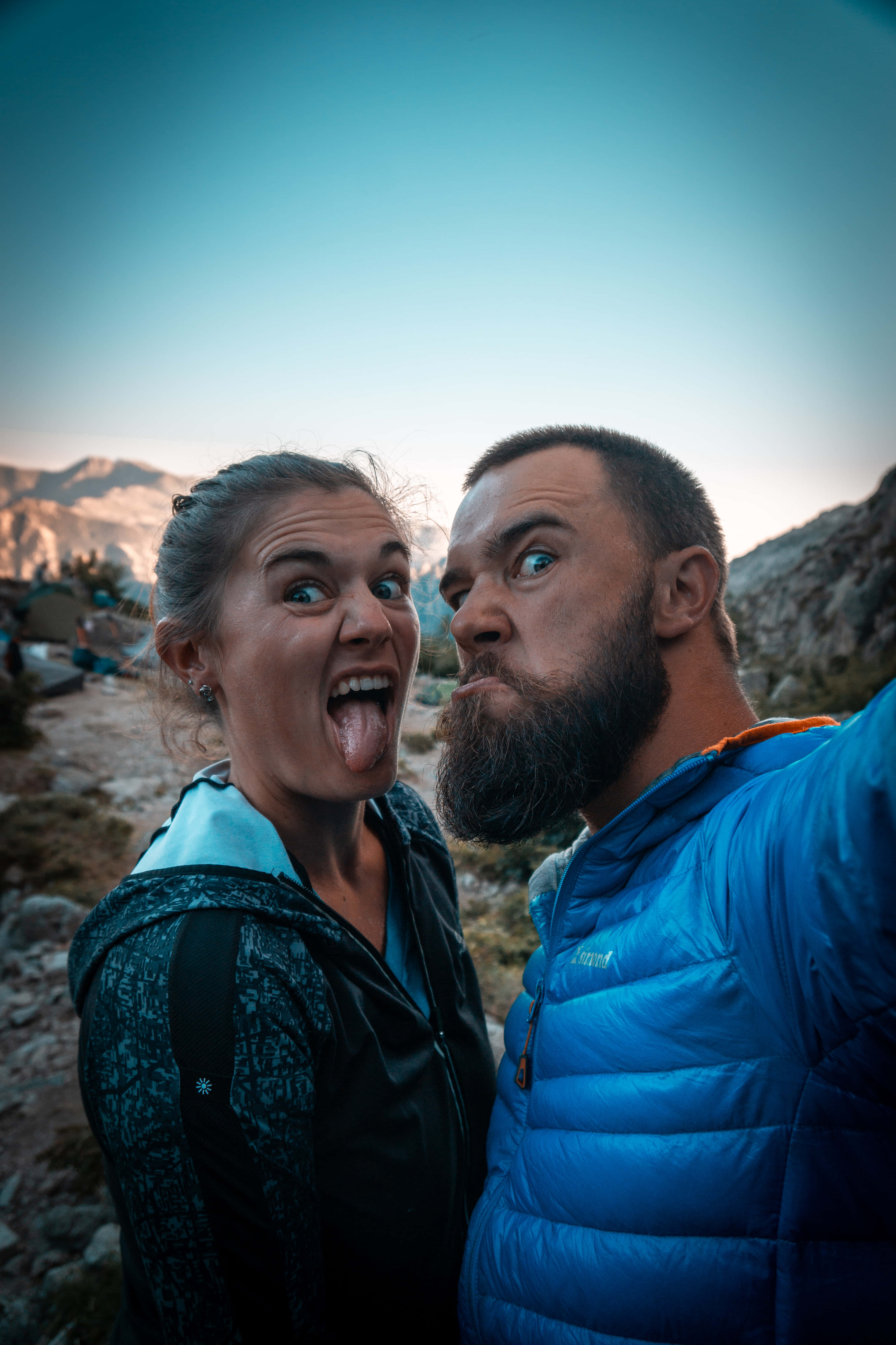 selfie 桌布 壁紙 — 兩名穿著登山裝備的遠足者，在崎嶇的山峰和柔和的暮色天空背景下，為自拍做出滑稽愚蠢的表情。