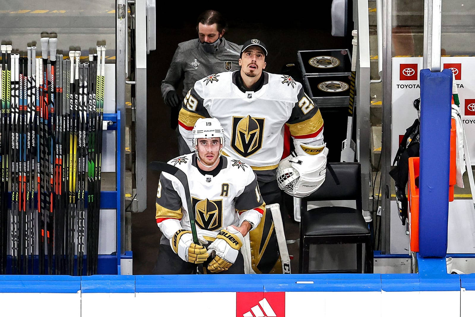 hockey 桌布 壁紙 — 兩名穿著白金色球衣的維加斯黃金騎士冰球球員坐在板凳區，手持球棍，身後站著一名隊友。