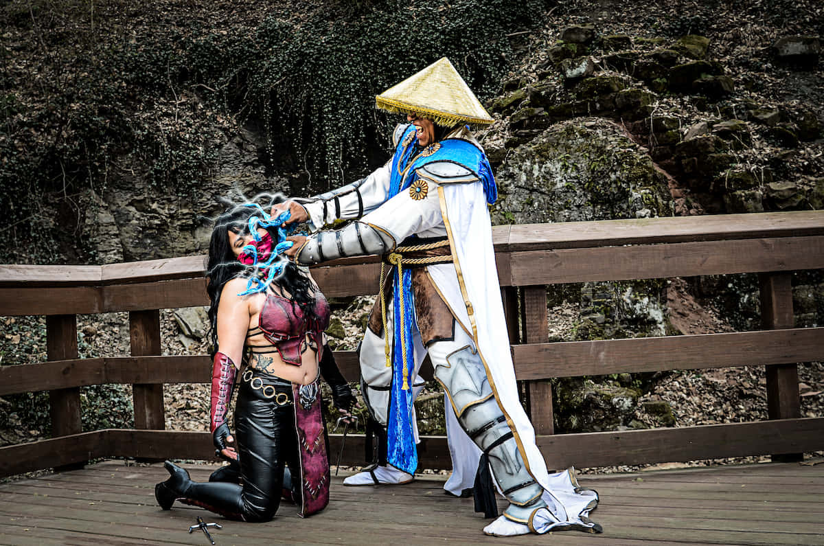 Mortal Kombat Cosplays 桌布 壁紙 — 兩名穿著精緻Mortal Kombat服裝的角色扮演者在木橋上戲劇性地擺姿勢，背後是岩石峭壁。