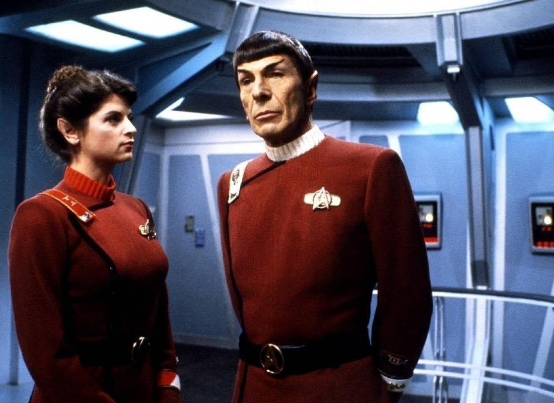 Spock 桌布 壁紙 — 兩名穿著紅色制服的星際爭霸戰船員站在未來感的太空船走廊，有藍色牆壁和發光面板。