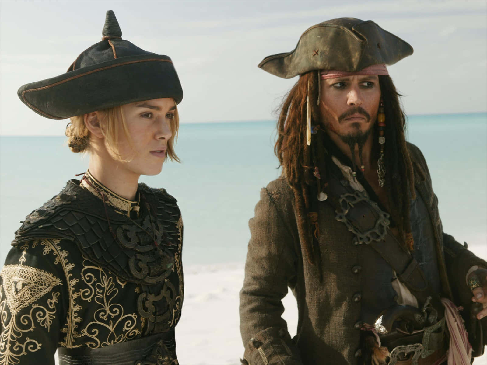 Pirates Of The Caribbean 桌布 壁紙 — 兩名穿著華麗服裝的海盜站在陽光明媚的海灘上，身後是碧綠的海洋。