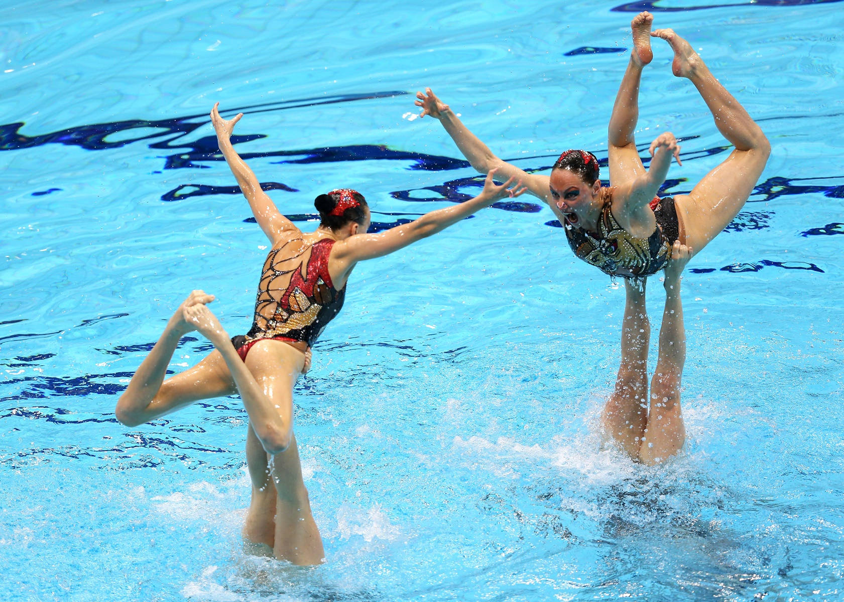 Swimming 桌布 壁紙 — 兩名穿著華麗服裝的韻律泳選手在充滿活力的藍色水中做出雙腿分開、雙臂伸展的動態姿勢。