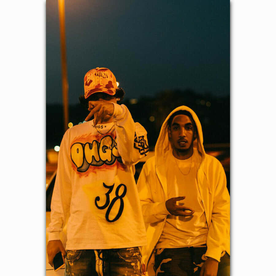 Shoreline Mafia 桌布 壁紙 — 兩名穿著街頭服的年輕男子在溫暖的街燈下，以黑暗的城市夜景為背景擺姿勢。