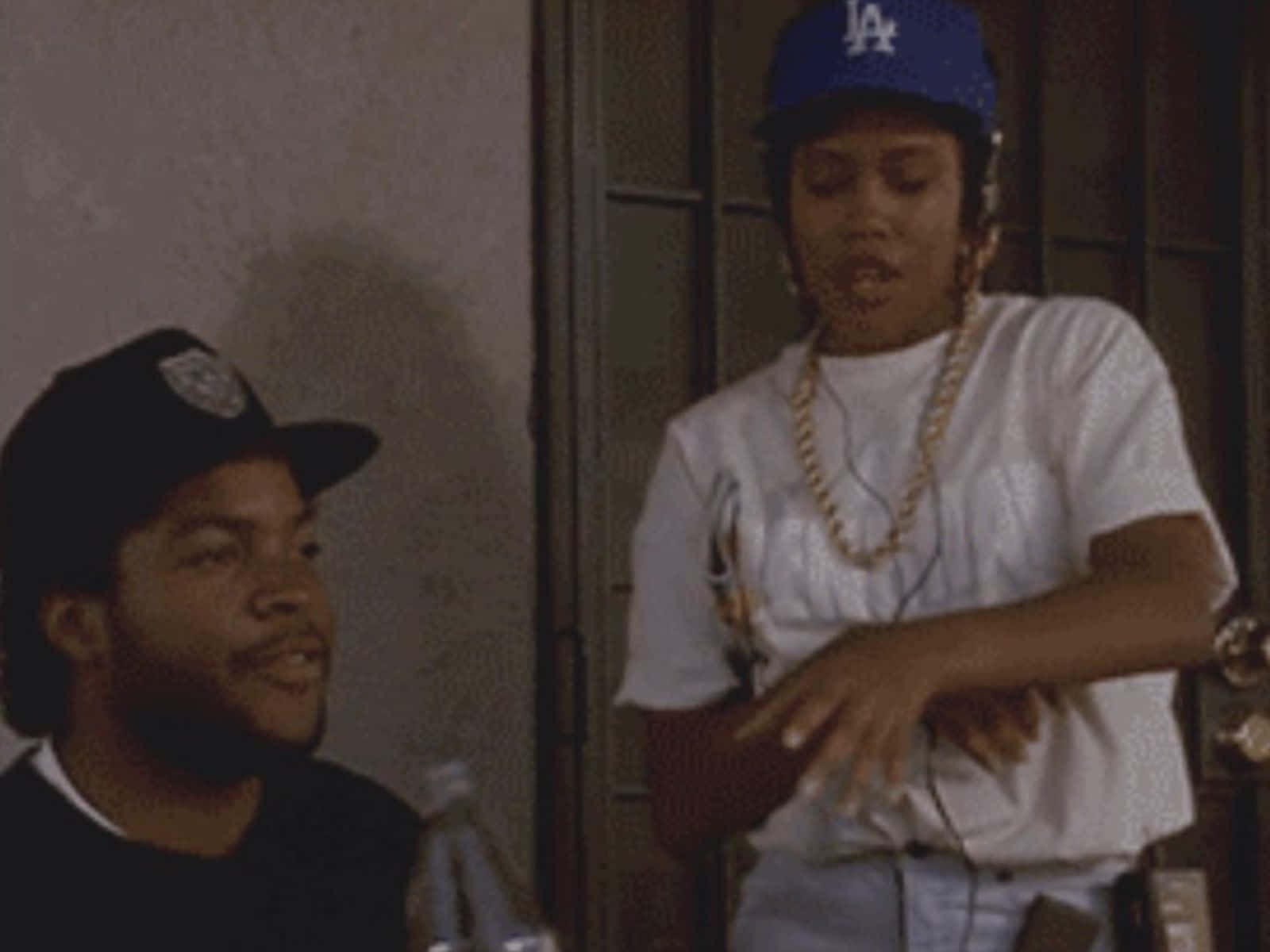 Boyz N The Hood 桌布 壁紙 — 兩名穿著街頭服飾的男子，一人戴藍色LA帽和金色鏈條，另一人戴黑色帽，兩人均處於昏暗的室內環境。