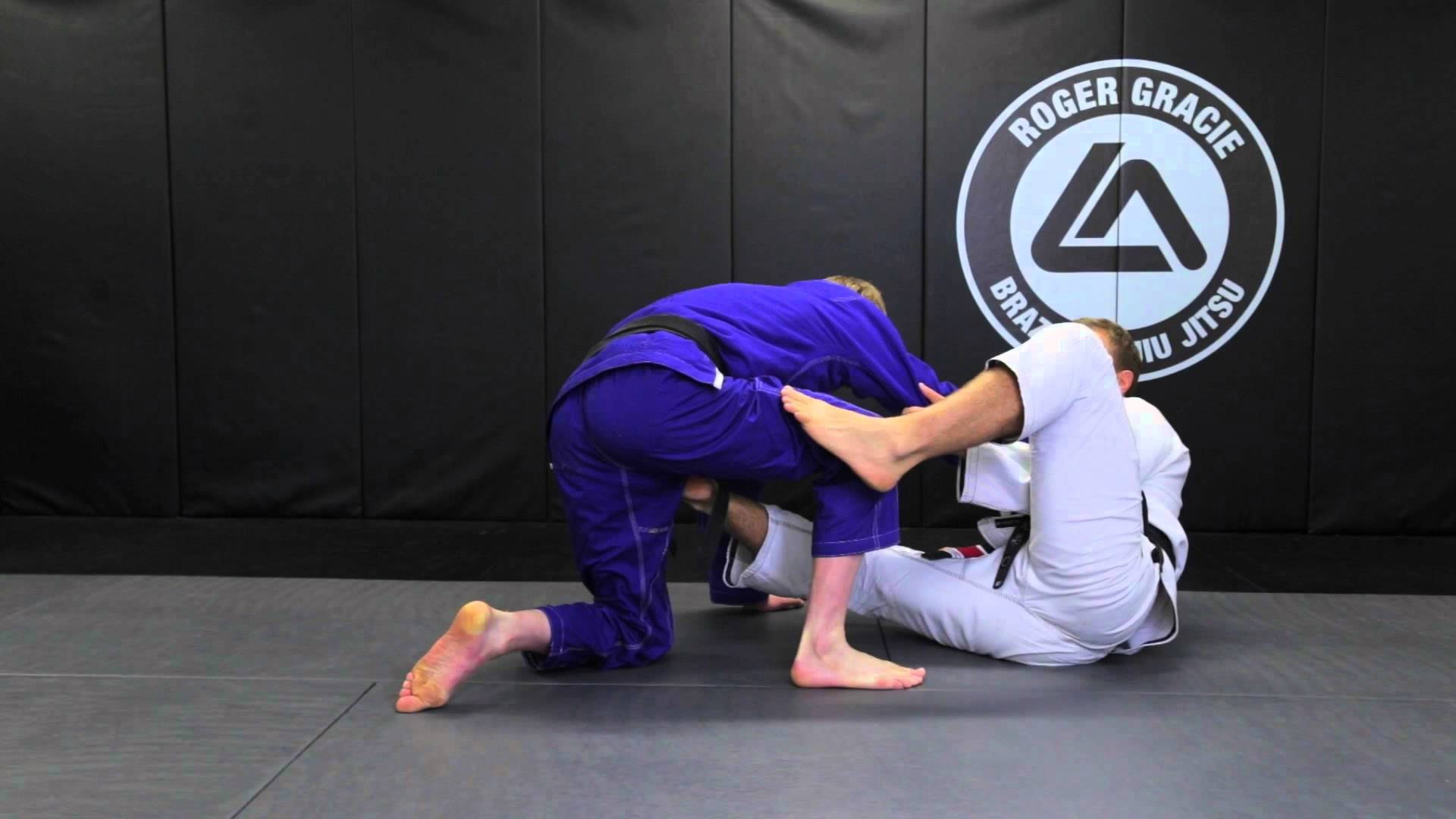 martial arts 桌布 壁紙 — 兩名穿著道服的武術家在墊上激烈纏鬥，身後牆上掛有Roger Gracie BJJ標誌。