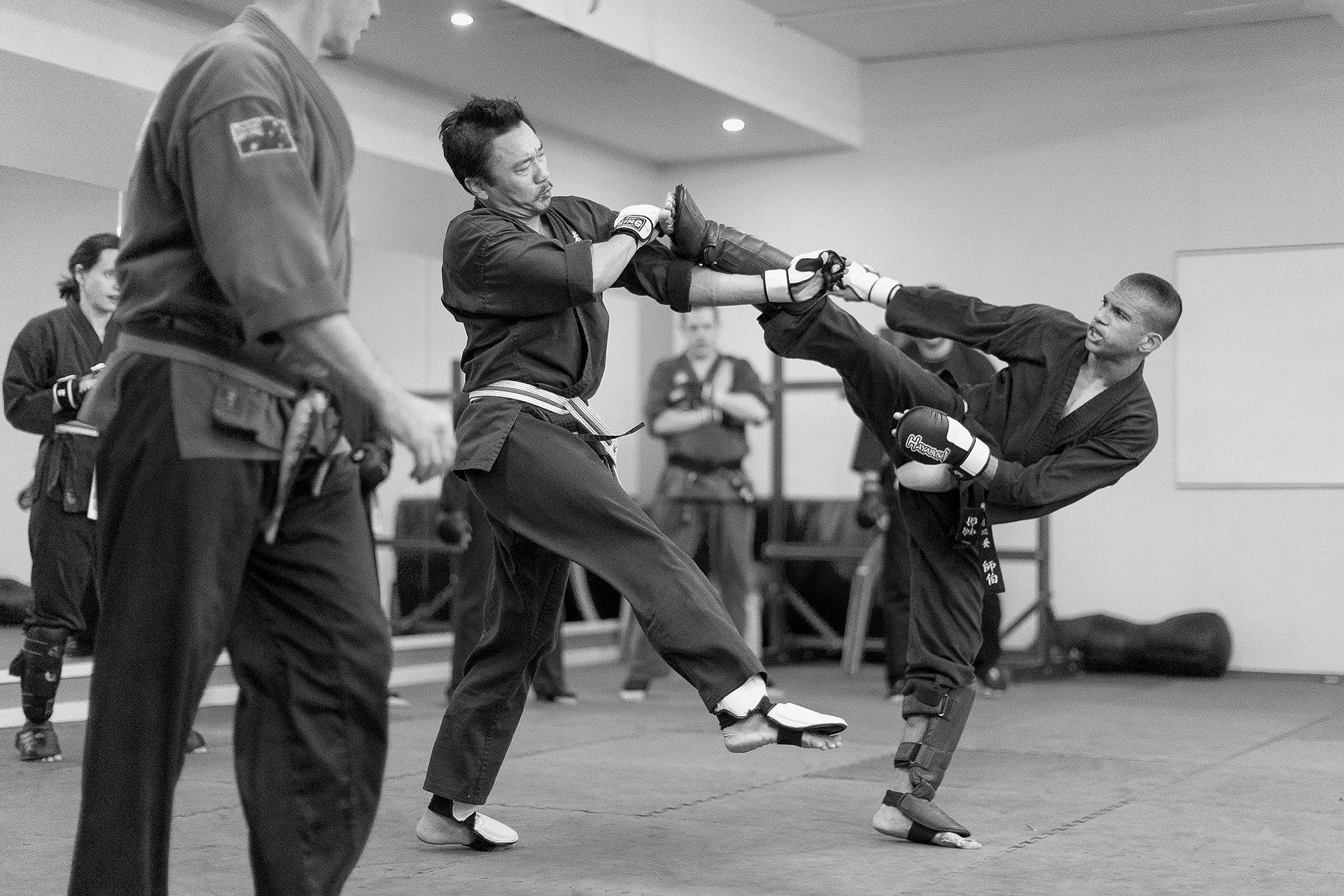 martial arts 桌布 壁紙 — 兩名穿著道服的武術家在道場內進行動態踢腿訓練，其他人正在觀看。