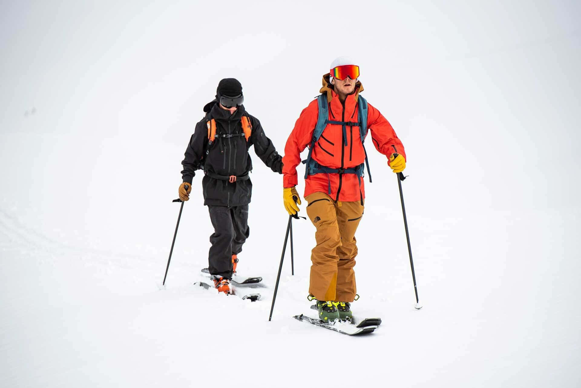 ski 桌布 壁紙 — 兩名穿著鮮豔裝備的滑雪者，在陰天之下穿越廣闊的雪地。