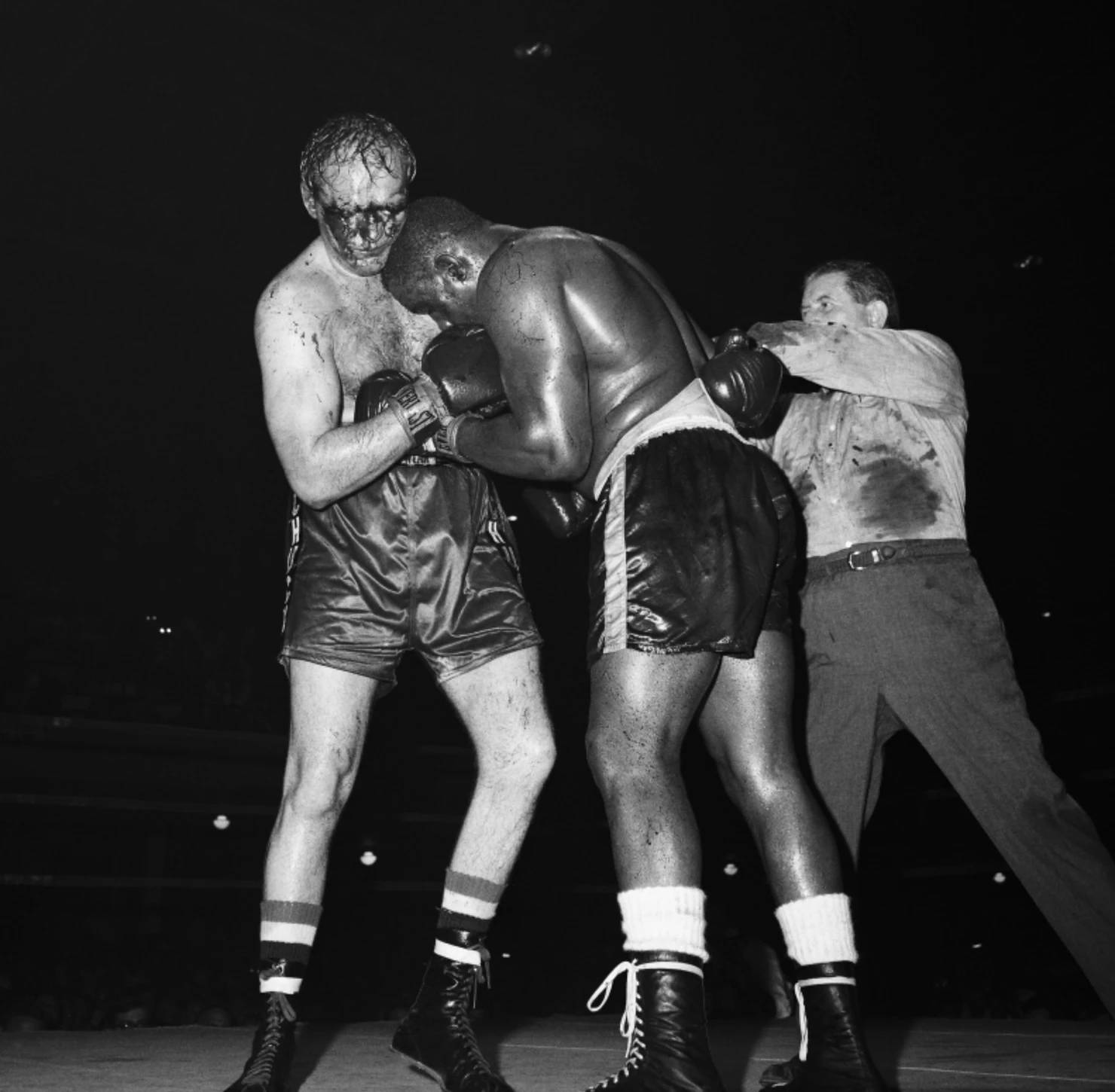 Boxing 桌布 壁紙 — 兩名筋疲力竭的拳擊手在昏暗的擂台上激烈纏鬥，裁判在殘酷的夜間比賽中介入。