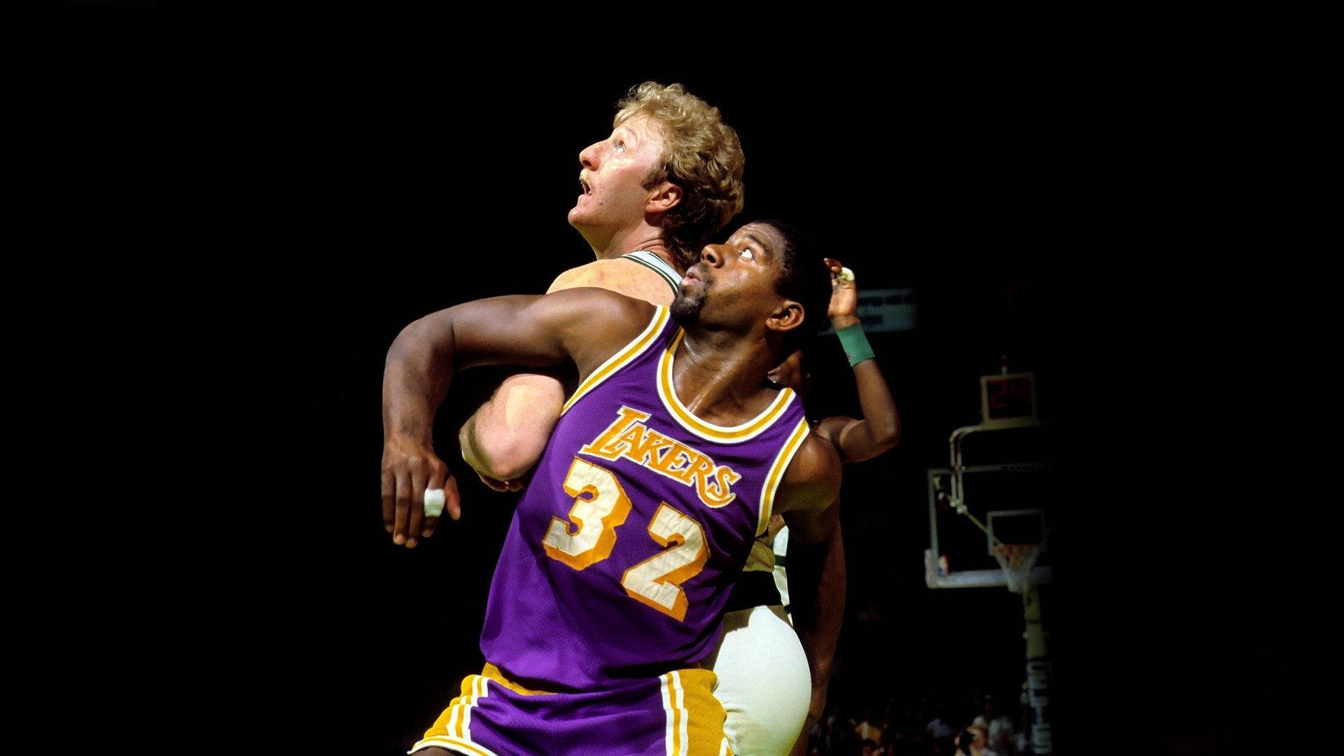 Magic Johnson 桌布 壁紙 — 兩名籃球運動員在明亮的場館燈光下，在黑色背景前激烈爭奪籃板球。