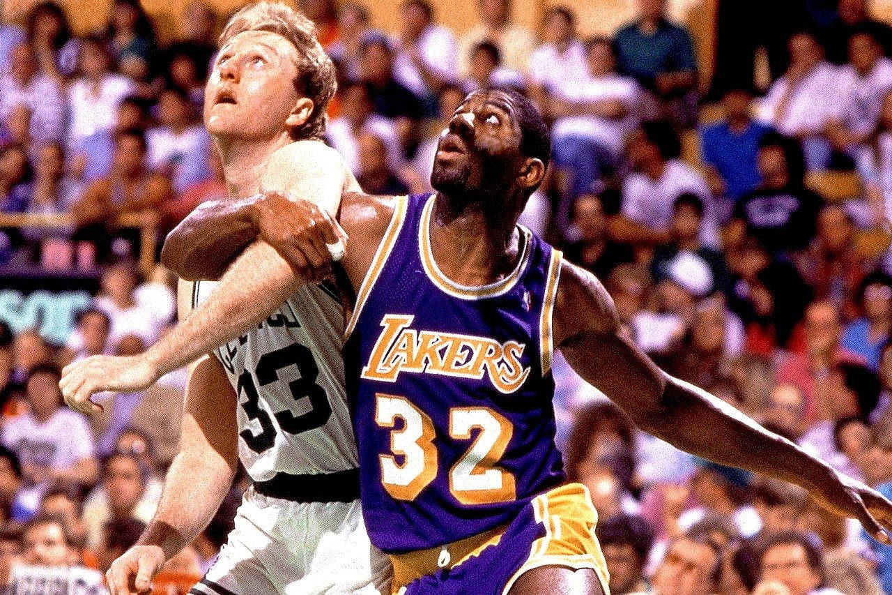 Magic Johnson 桌布 壁紙 — 兩名籃球運動員在明亮的燈光下，於擁擠的場館中進行高風險比賽時激烈競爭。