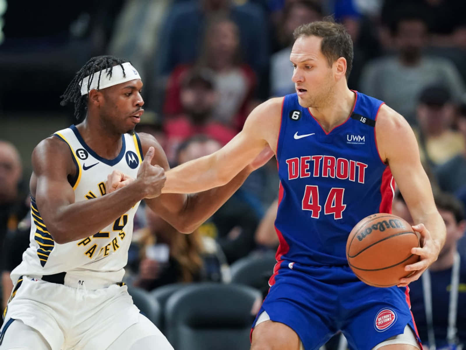 buddy hield 桌布 壁紙 — 兩名籃球運動員在比賽中激烈競爭，一名身穿藍色底特律球衣運球，另一名身穿白色球衣緊密防守。
