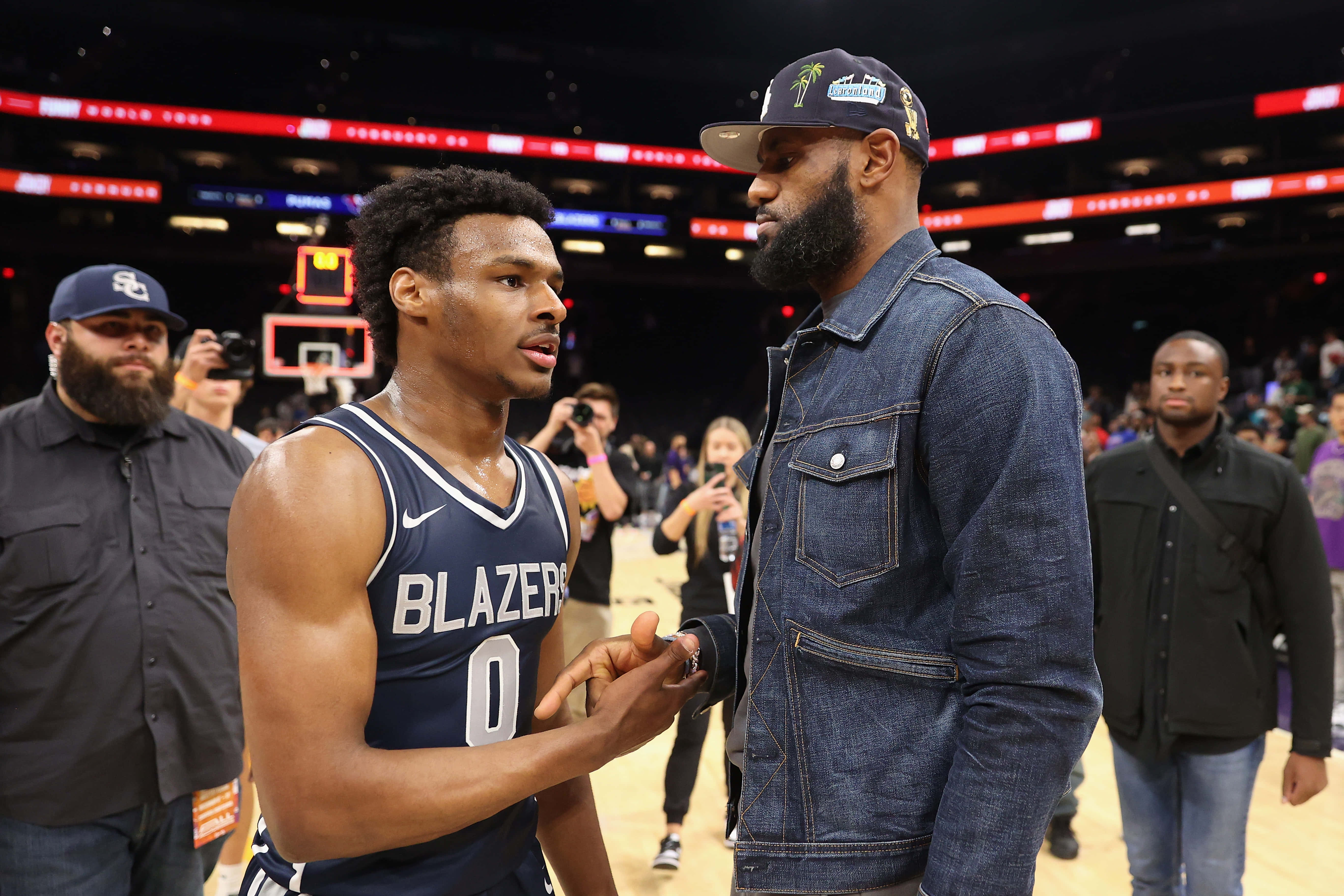 Bronny James 桌布 壁紙 — 兩名籃球運動員在燈光明亮的球場上激烈交談，周圍是球迷和攝影師。