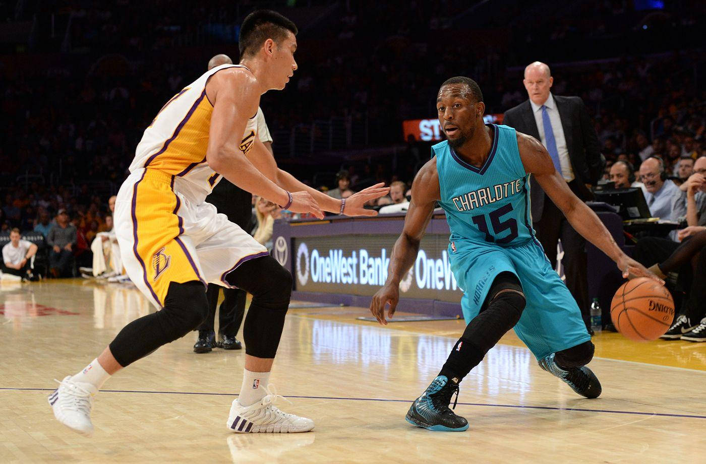 Kemba Walker 桌布 壁紙 — 兩名籃球運動員在燈光明亮的球場上激烈競爭，一名身穿黃白球衣防守，另一名身穿青綠色球衣運球。