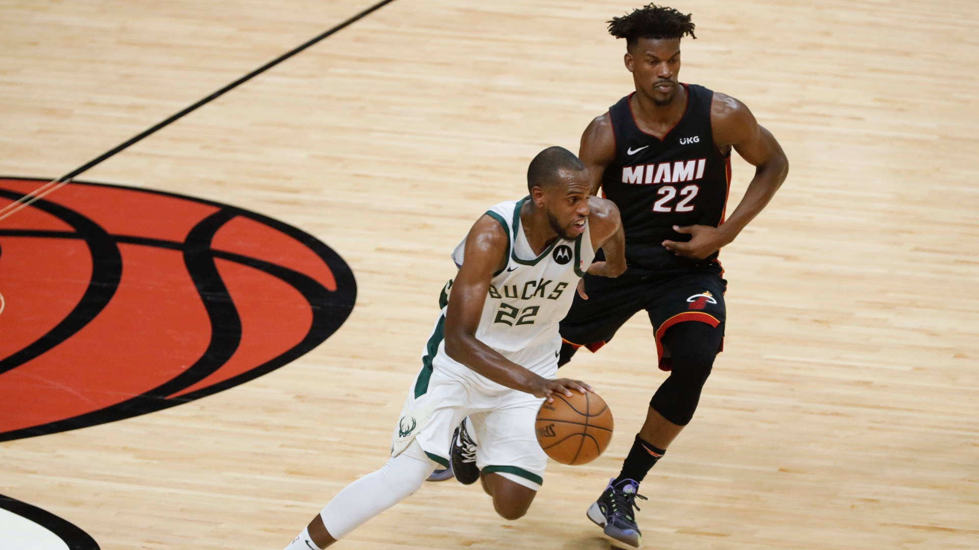 Khris Middleton 桌布 壁紙 — 兩名籃球運動員在硬木球場上比賽，其中一人運球時受到防守，球場上有球隊標誌。