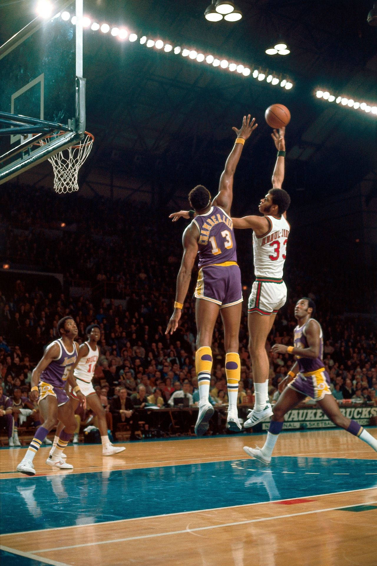 Kareem 桌布 壁紙 — 兩名籃球運動員在緊張的空中對抗中跳向籃框，場館燈光下，擠滿觀眾觀看。