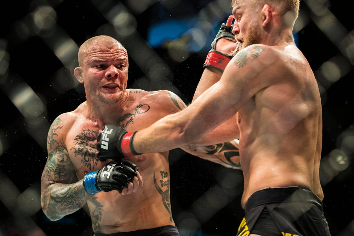 MMA 桌布 壁紙 — 兩名紋身MMA拳手在八角籠中交鋒，其中一人向對方臉部猛烈出拳。