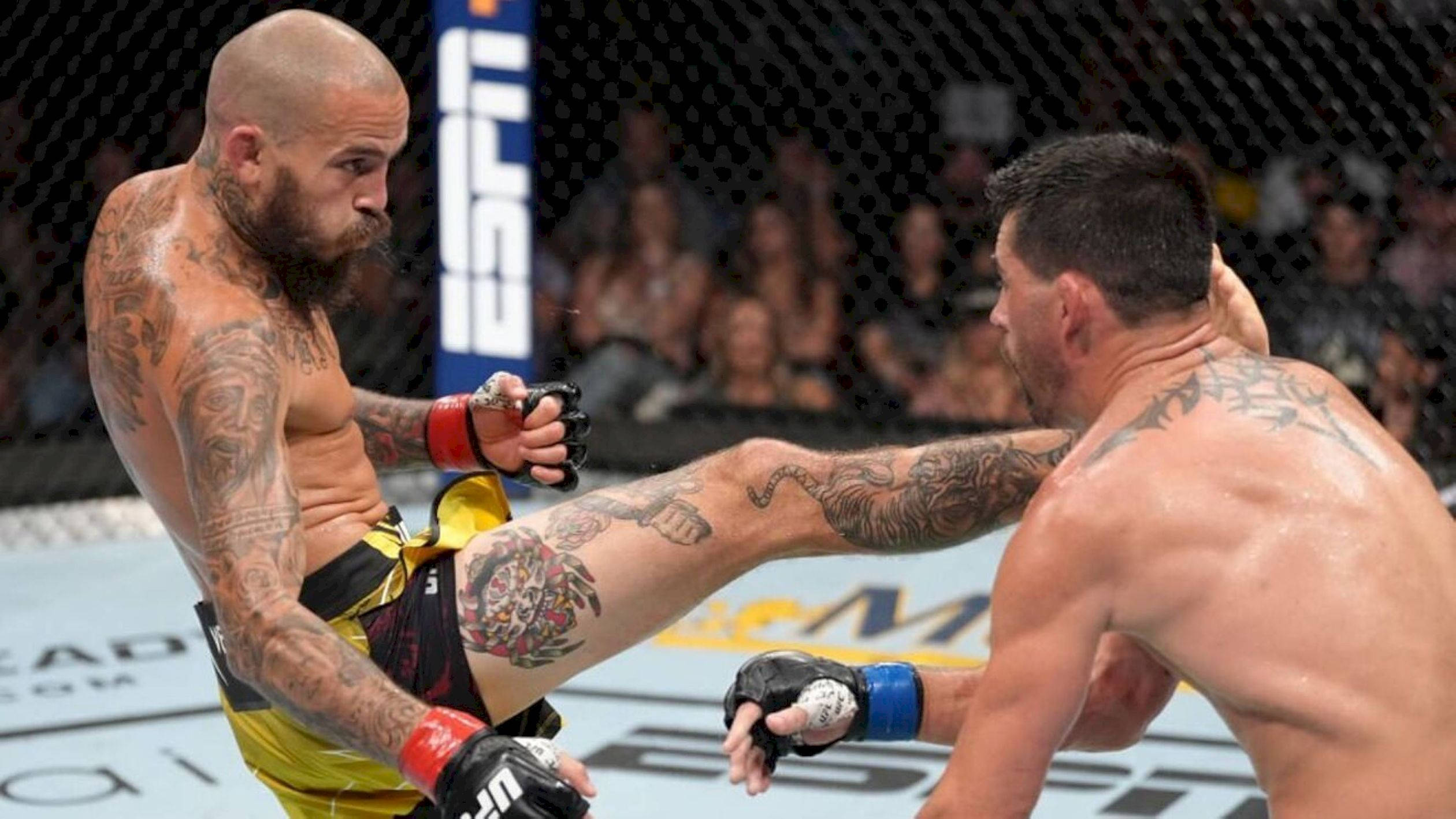 Champion 桌布 壁紙 — 兩名紋身MMA拳手在八角籠中交鋒，一人使出高踢，另一人在明亮的場館燈光下格擋。