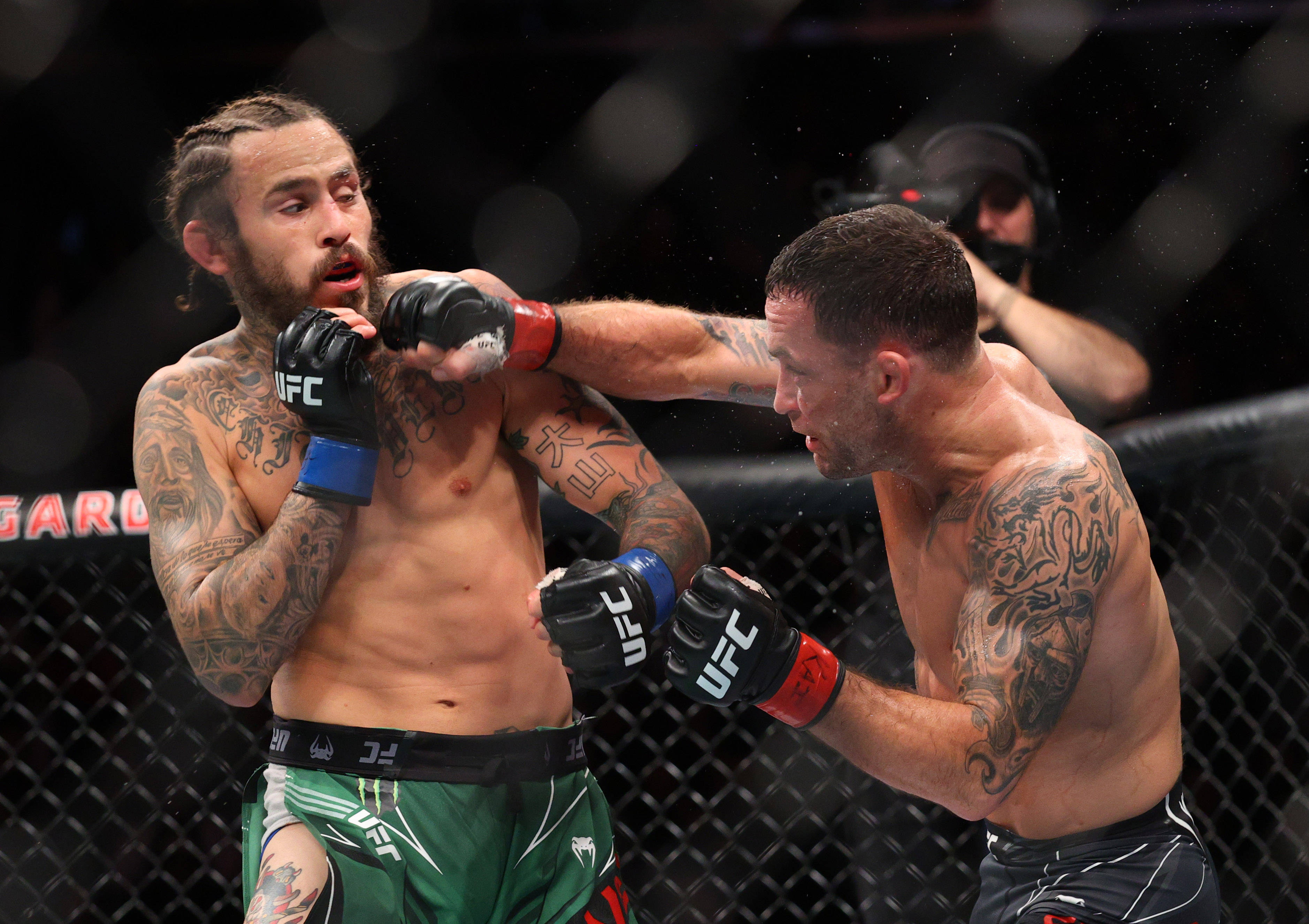 UFC 桌布 壁紙 — 兩名紋身MMA拳手在籠中激戰，一人揮拳，汗水在戲劇性的場館燈光下飛濺。