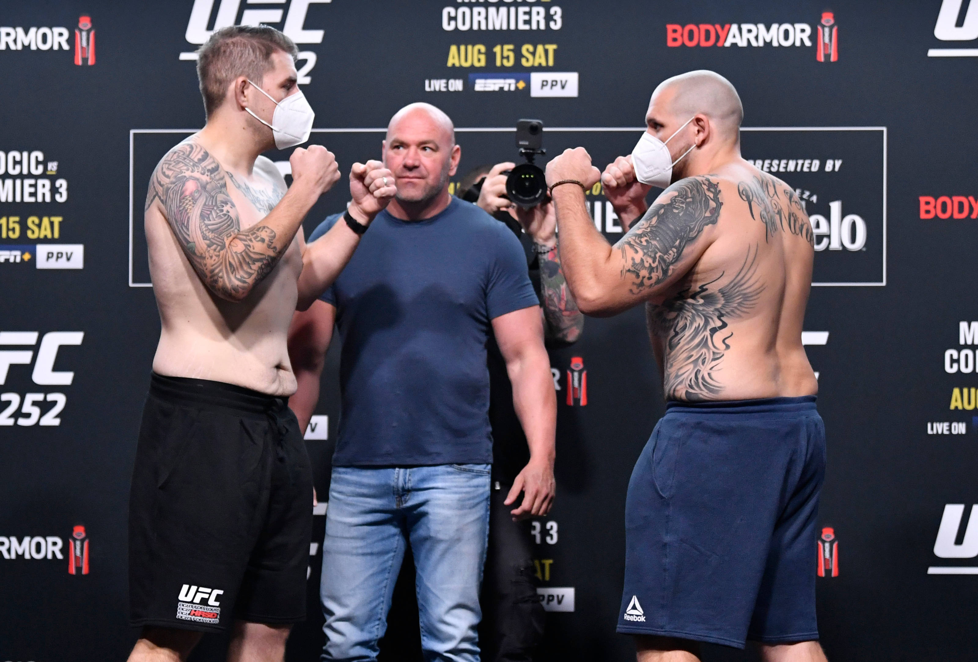 UFC 桌布 壁紙 — 兩名紋身UFC拳手戴著面具在稱重儀式上對峙，Dana White 在中間。