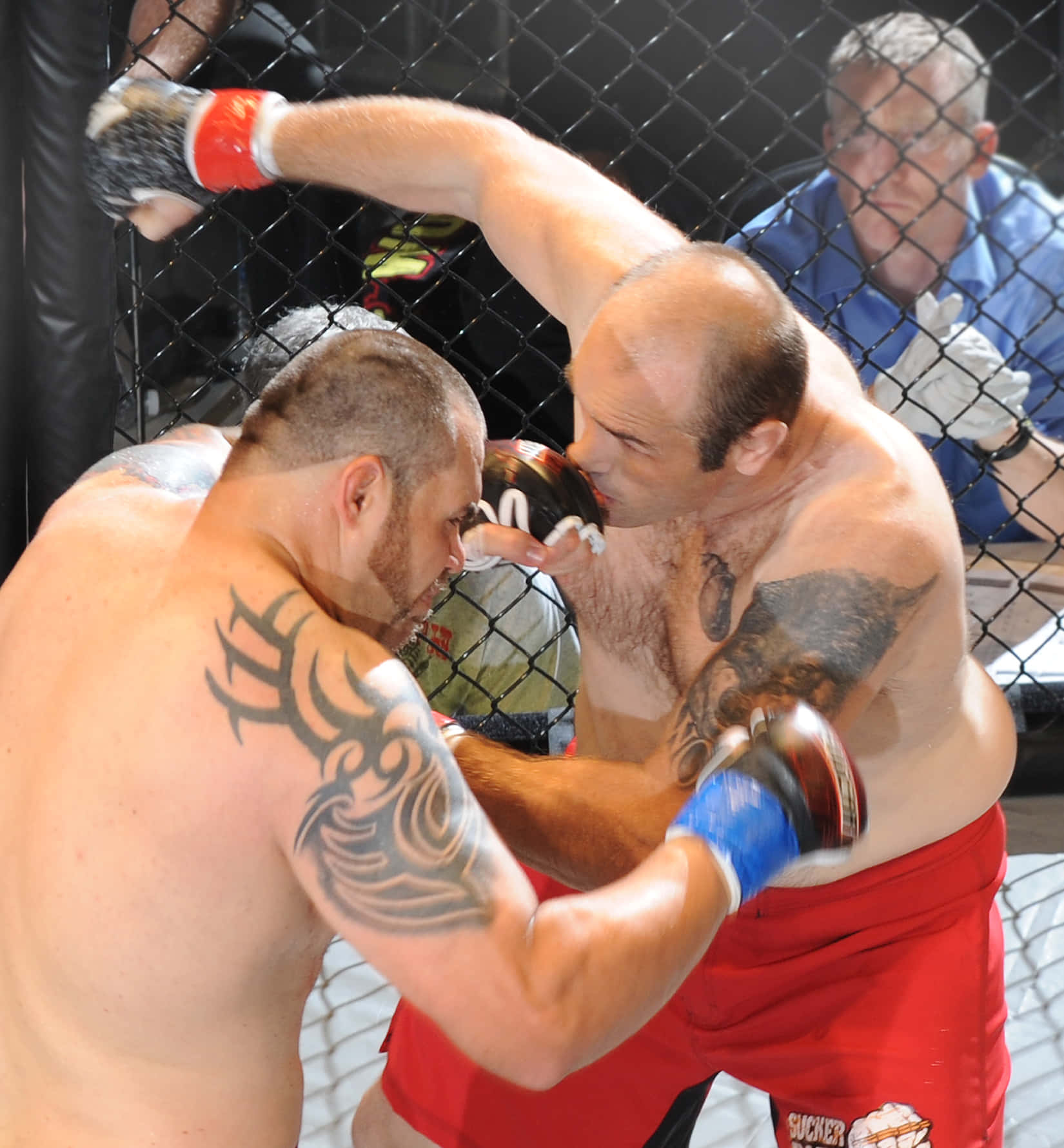 martial arts 桌布 壁紙 — 兩名紋身拳手在籠中交鋒，其中一人向對手面部猛烈出拳。