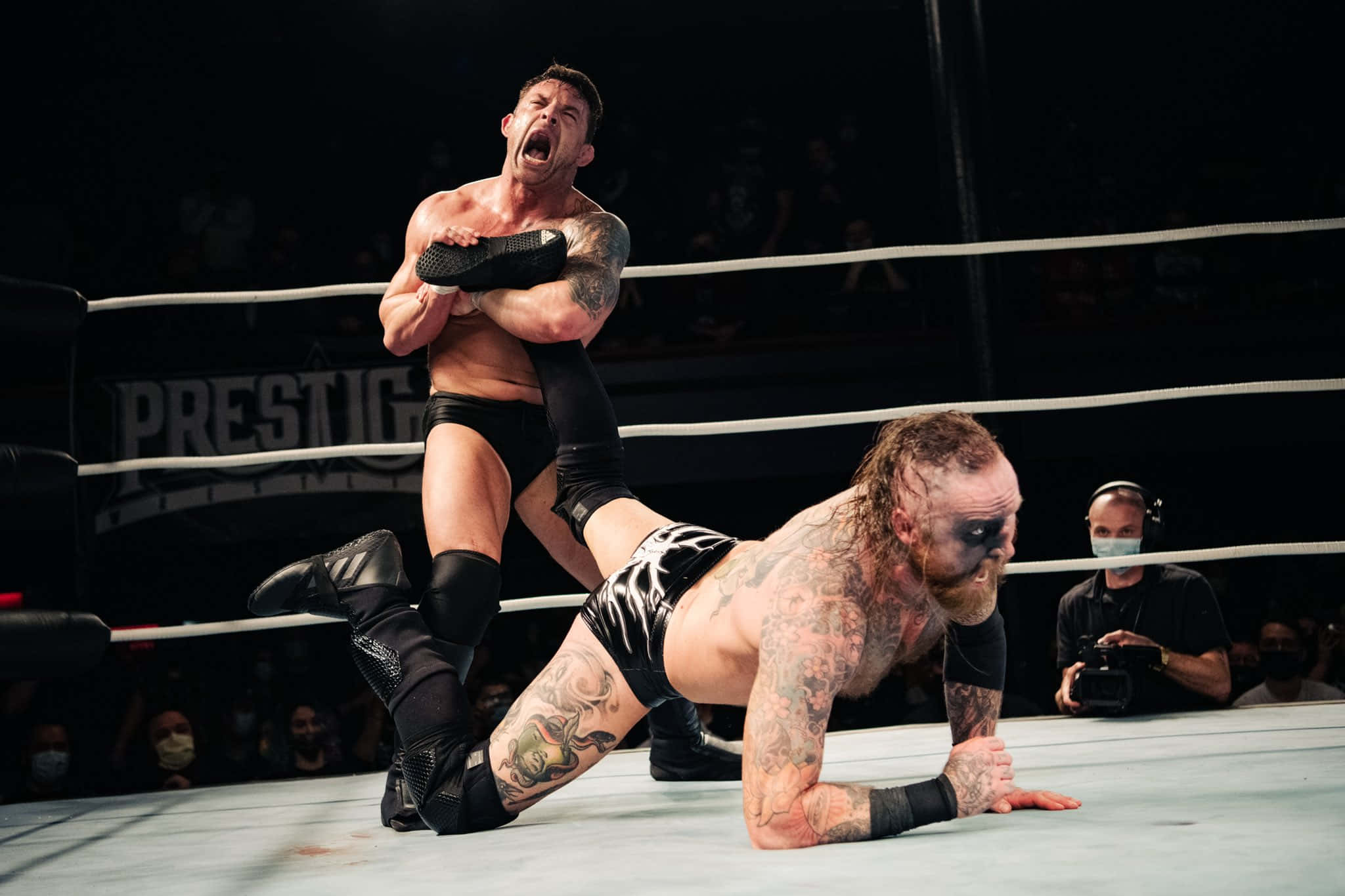 WWE 桌布 壁紙 — 兩名紋身摔角手在擂台上，其中一人將另一人舉起，在明亮的場館燈光下做出戲劇性的力量動作。