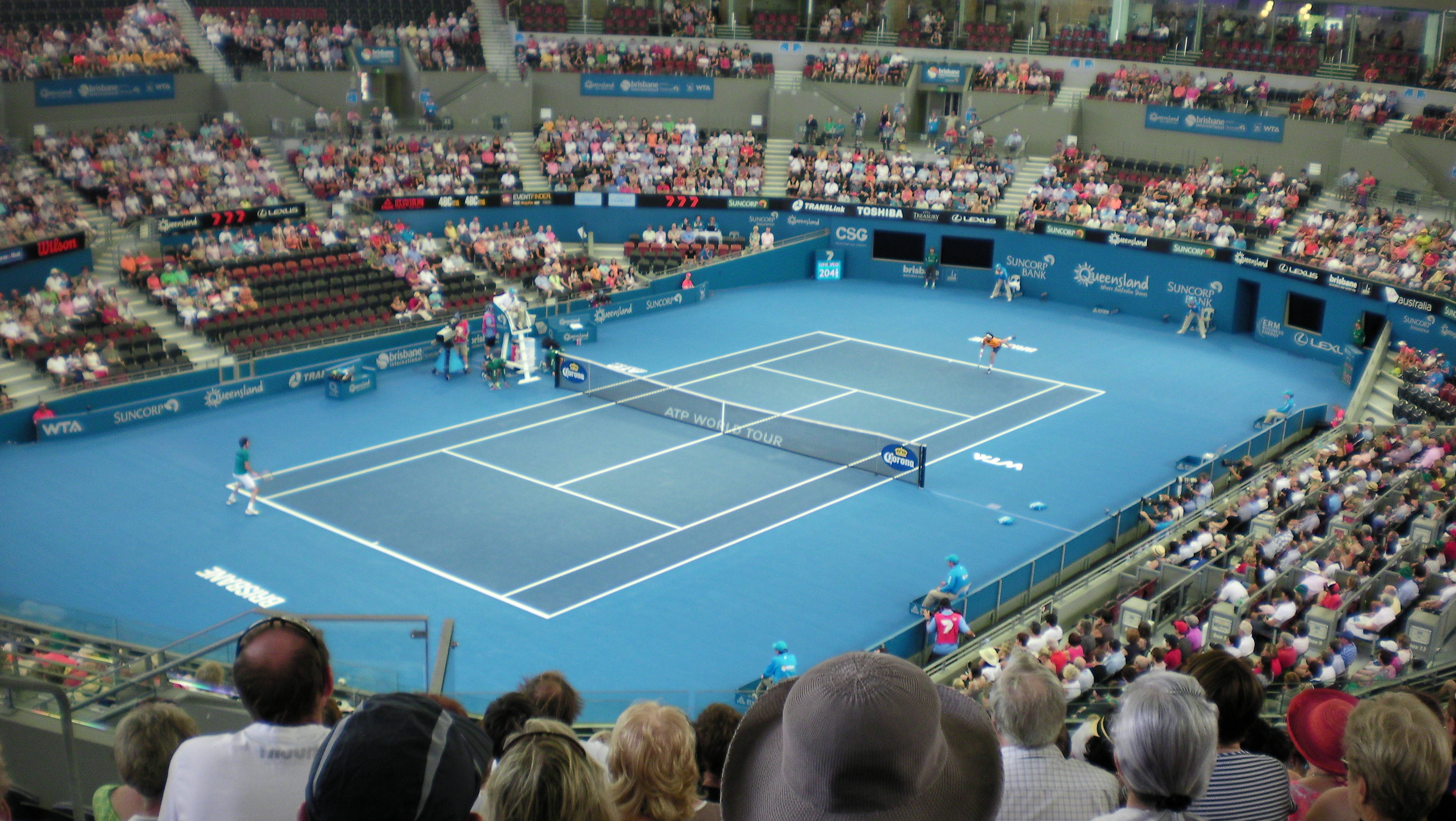 Tennis 桌布 壁紙 — 兩名網球運動員在明亮的體育場燈光下，在充滿活力的藍色硬地球場上比賽，觀眾席座無虛席。