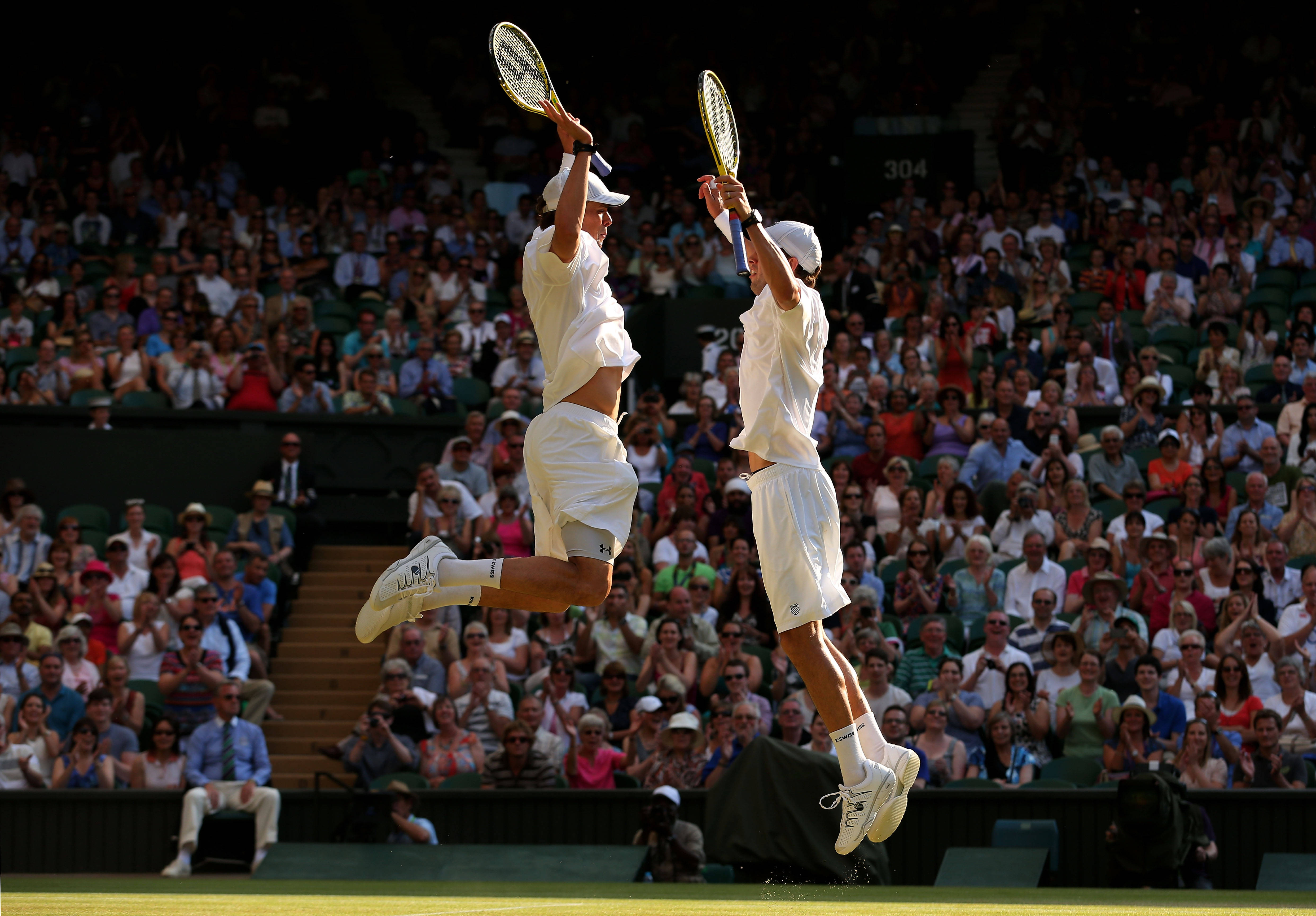 Tennis 桌布 壁紙 — 兩名網球選手在草地場上高舉球拍齊齊躍起，下方觀眾歡呼。