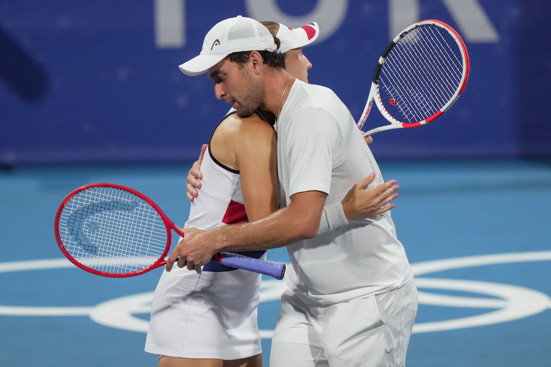 Tennis 桌布 壁紙 — 兩名網球選手在藍色硬地球場上，在明亮的體育場燈光下熱情擁抱。