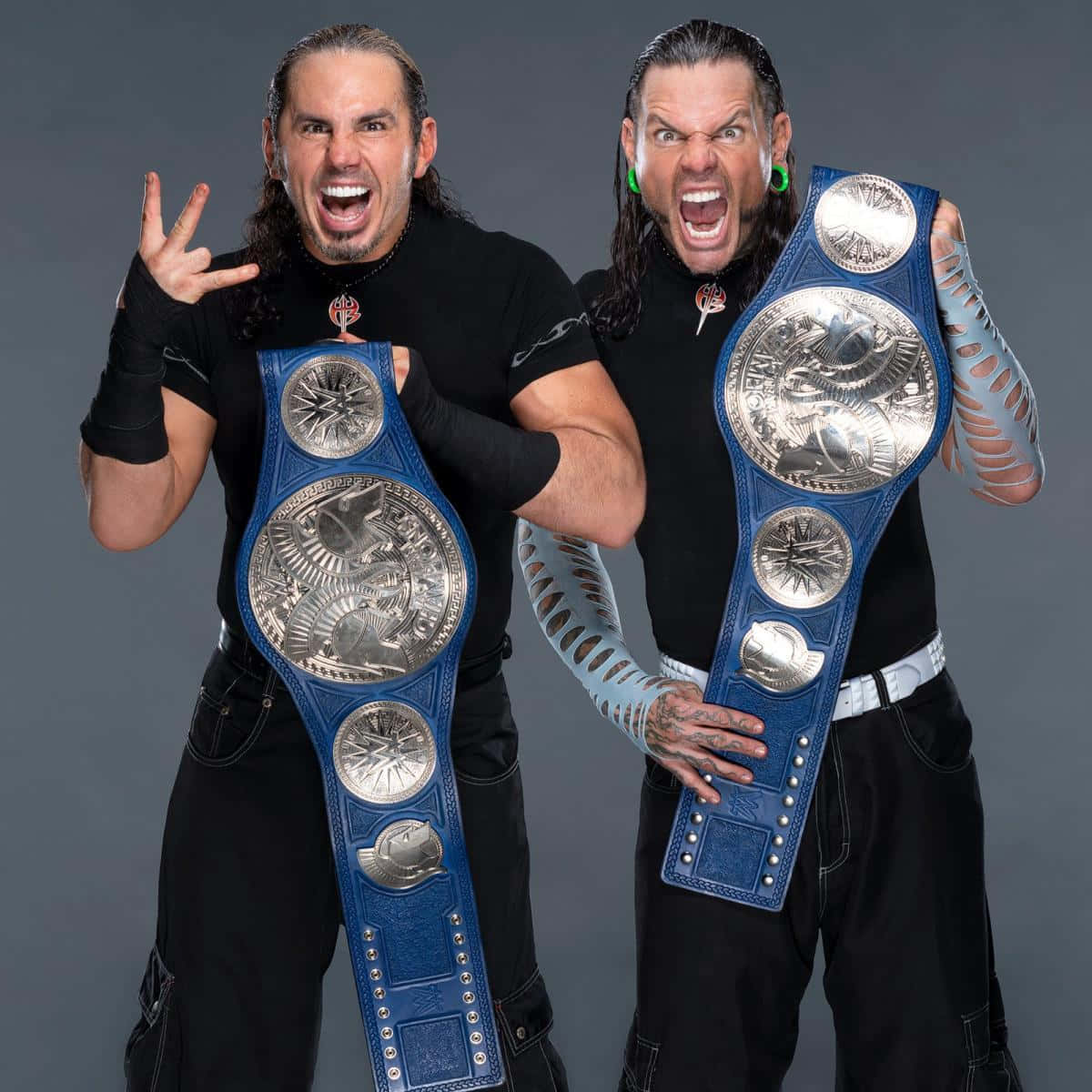 WWE 桌布 壁紙 — 兩名肌肉發達、長髮且有紋身的摔角手，在灰色攝影棚背景下手持藍色冠軍腰帶咆哮。