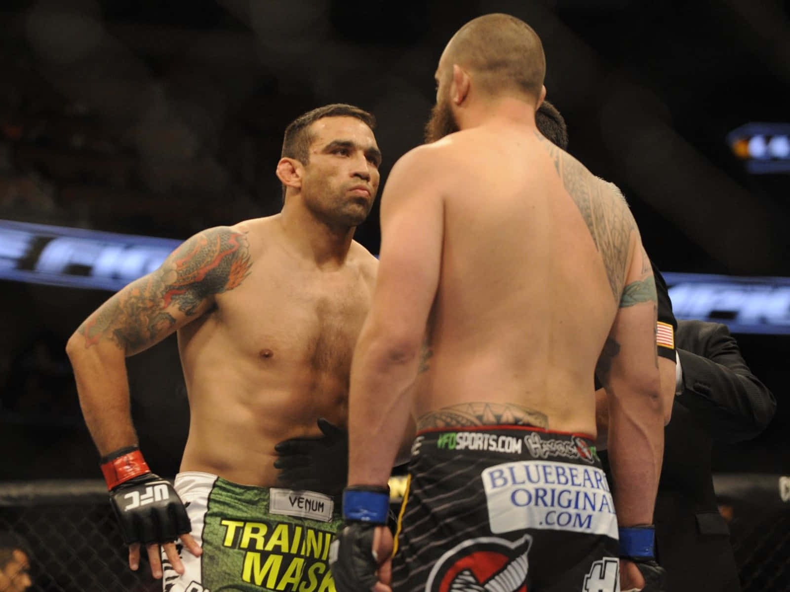 UFC 桌布 壁紙 — 兩名肌肉發達的MMA拳手在八角籠中對峙，專注力極強，紋身在明亮的場館燈光下清晰可見。