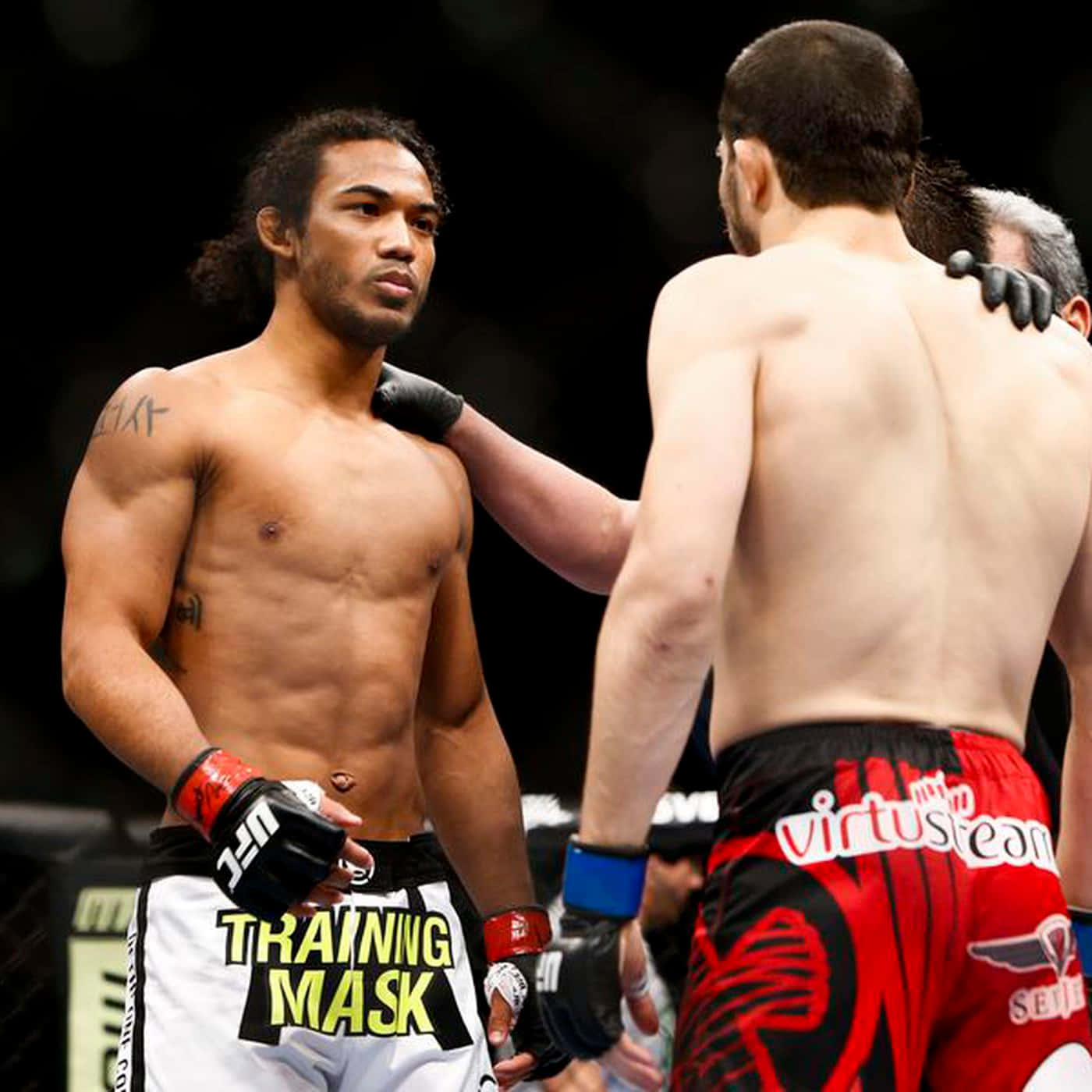 MMA 桌布 壁紙 — 兩名肌肉發達的MMA拳手在八角籠中對峙；一人穿著帶有訓練口罩文字的白色短褲，另一人穿著帶有virtus團隊標誌的紅黑短褲。
