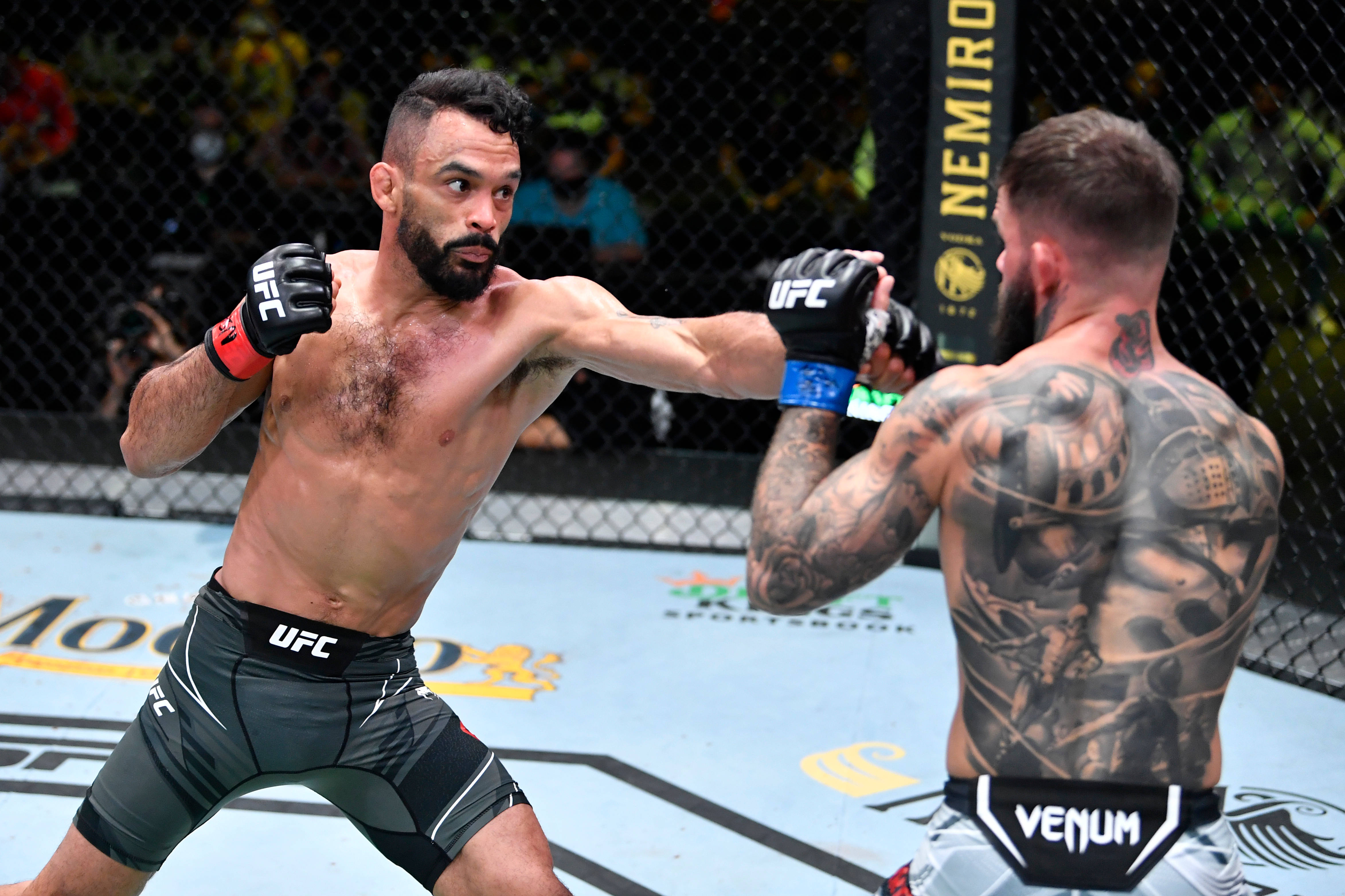 MMA 桌布 壁紙 — 兩名肌肉發達的MMA拳手在八角籠中交鋒，一人出拳，另一人以有刺青的手臂防守。