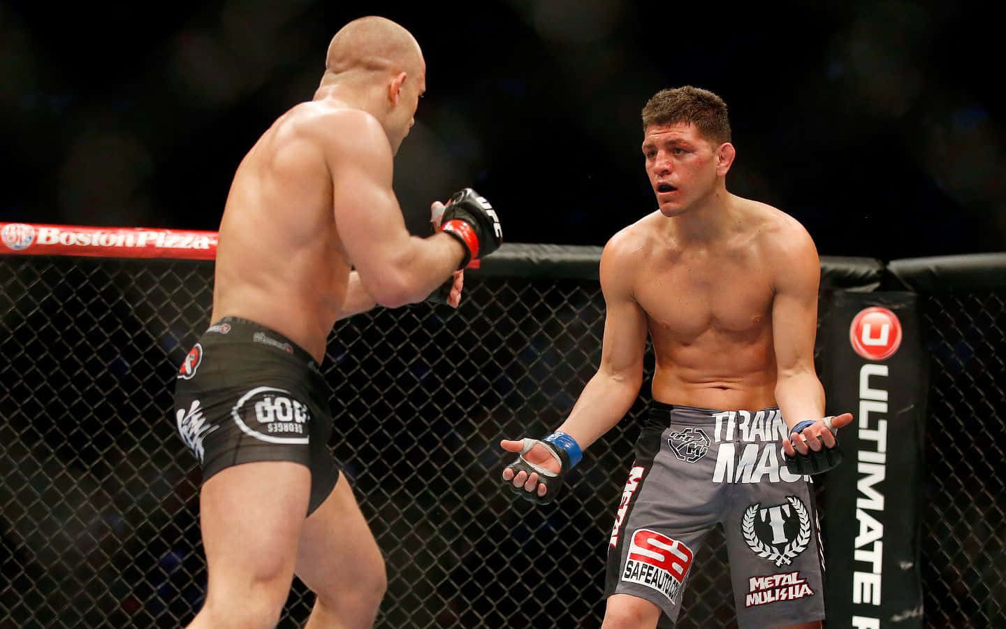 UFC 桌布 壁紙 — 兩名肌肉發達的MMA拳手在八角籠中對峙，一人揮拳，另一人驚訝反應。