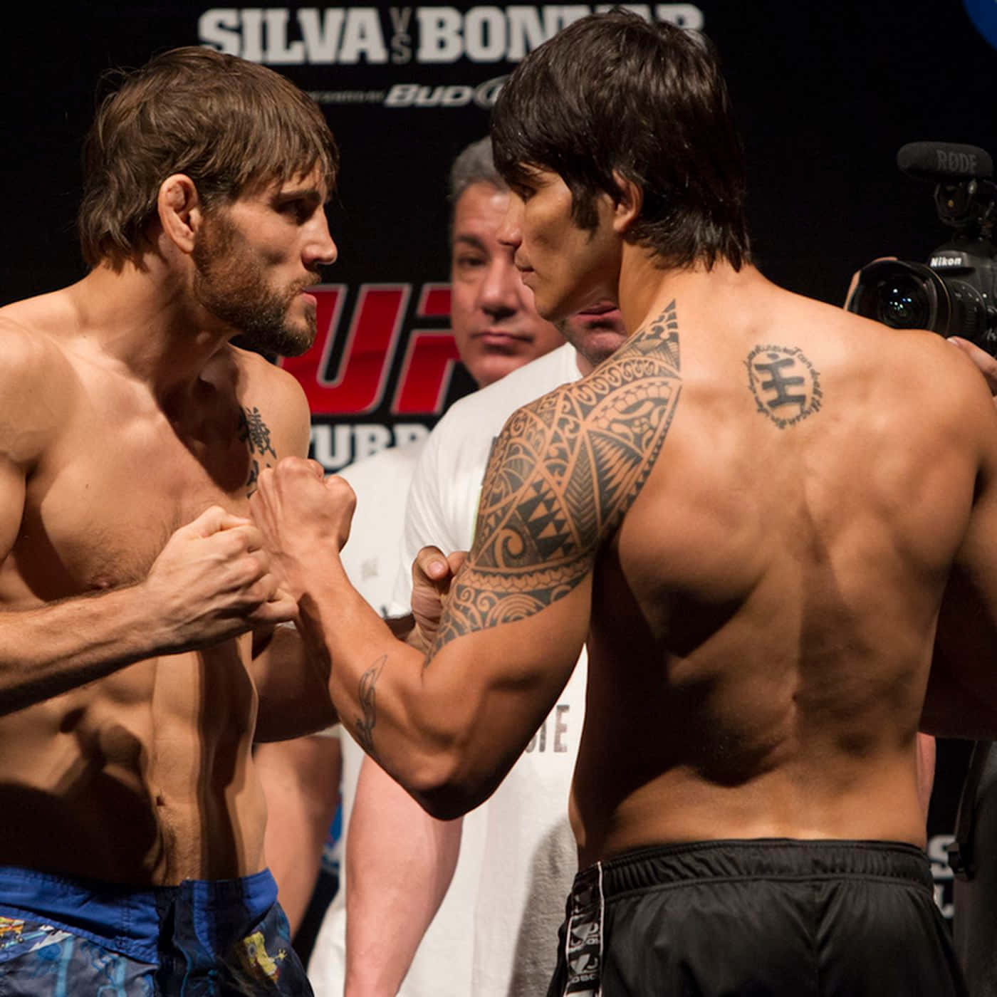 UFC 桌布 壁紙 — 兩名肌肉發達的MMA拳手在明亮的場館燈光下，於緊張的賽前對峙中鎖住拳頭。