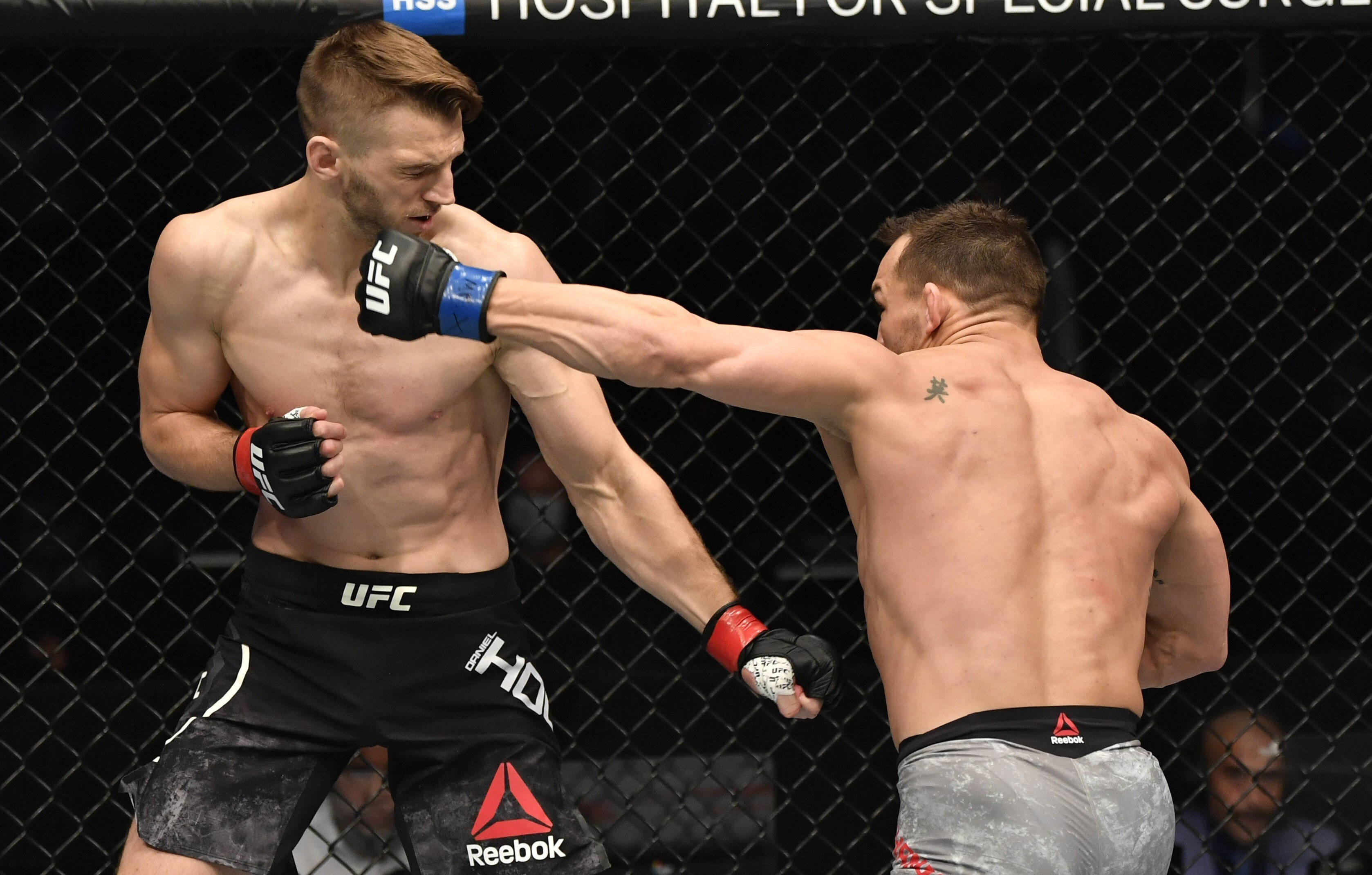 UFC 桌布 壁紙 — 兩名肌肉發達的MMA拳手在激烈的鐵籠賽中交鋒，其中一人打出強力一拳。
