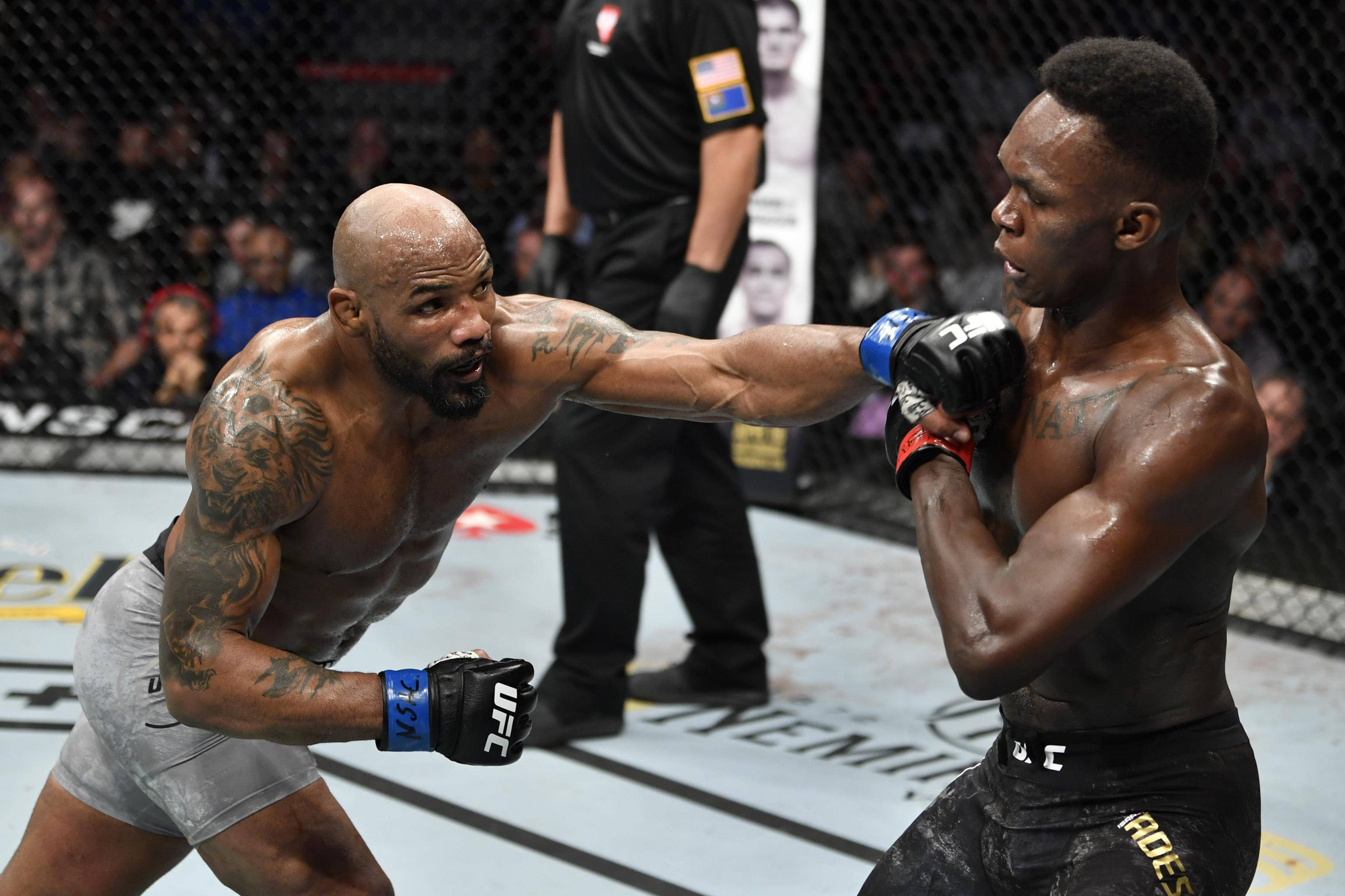 Adesanya 桌布 壁紙 — 兩名肌肉發達的MMA拳手在籠中交鋒，一人打出強力一拳，另一人阻擋。