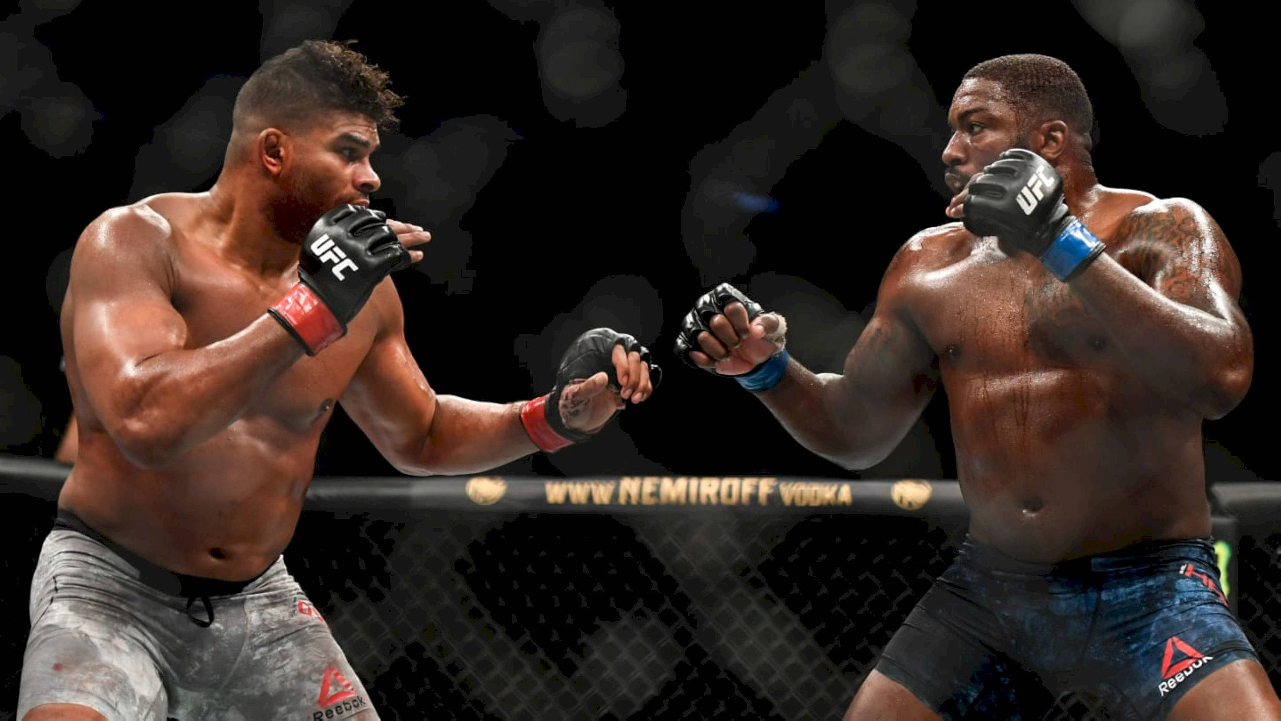 UFC 桌布 壁紙 — 兩名肌肉發達的MMA拳手在籠中激烈交鋒，汗水飛濺，在明亮的場館燈光下互相出拳。